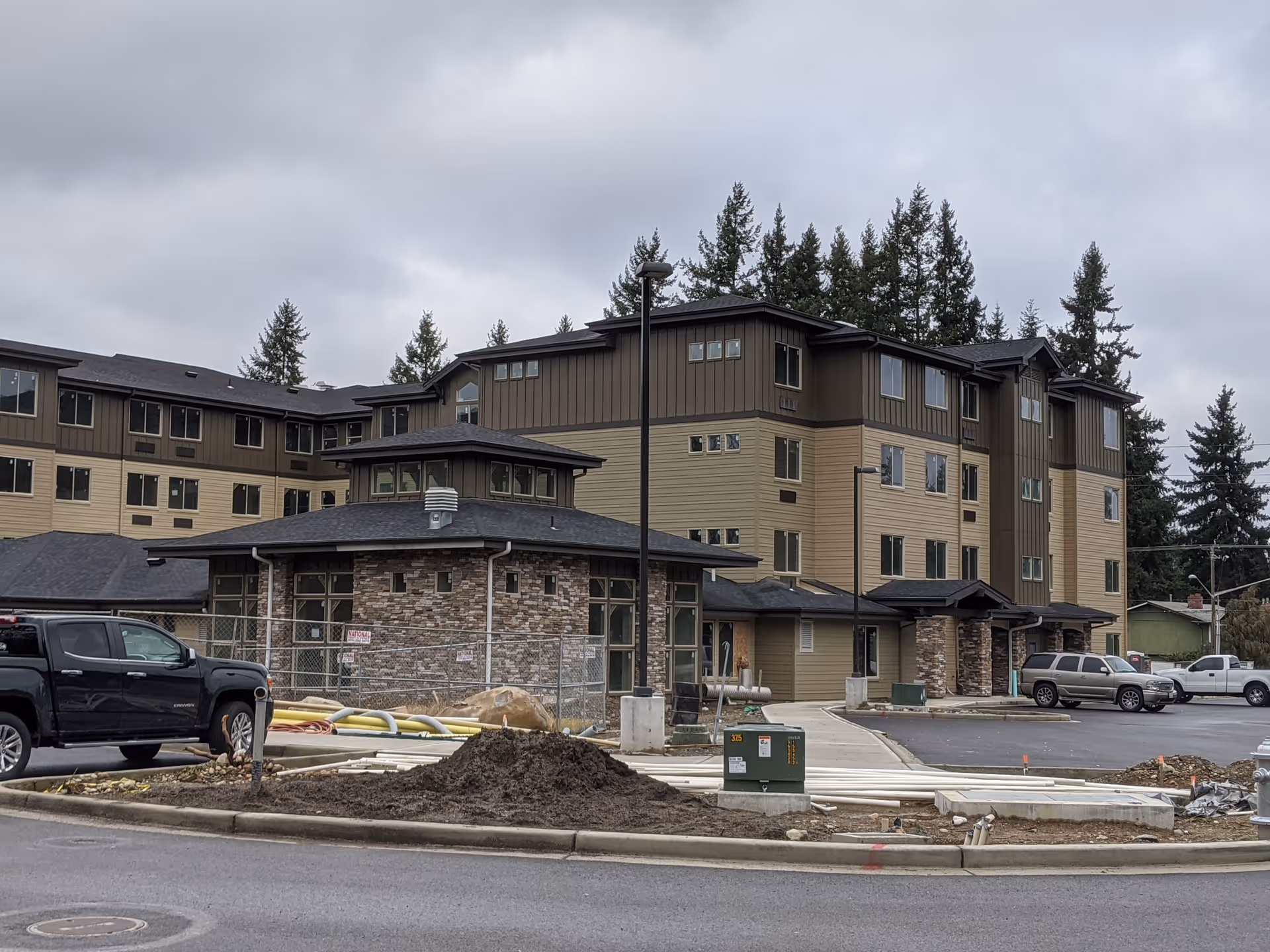 Modern multi-story senior living facility under construction, with brown siding and parked vehicles.
