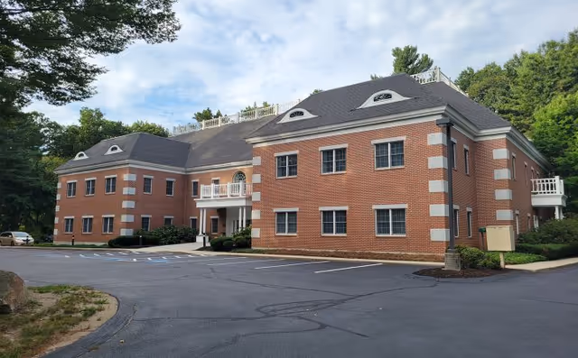 Brick senior housing building with entrance, surrounded by trees and a paved parking lot.