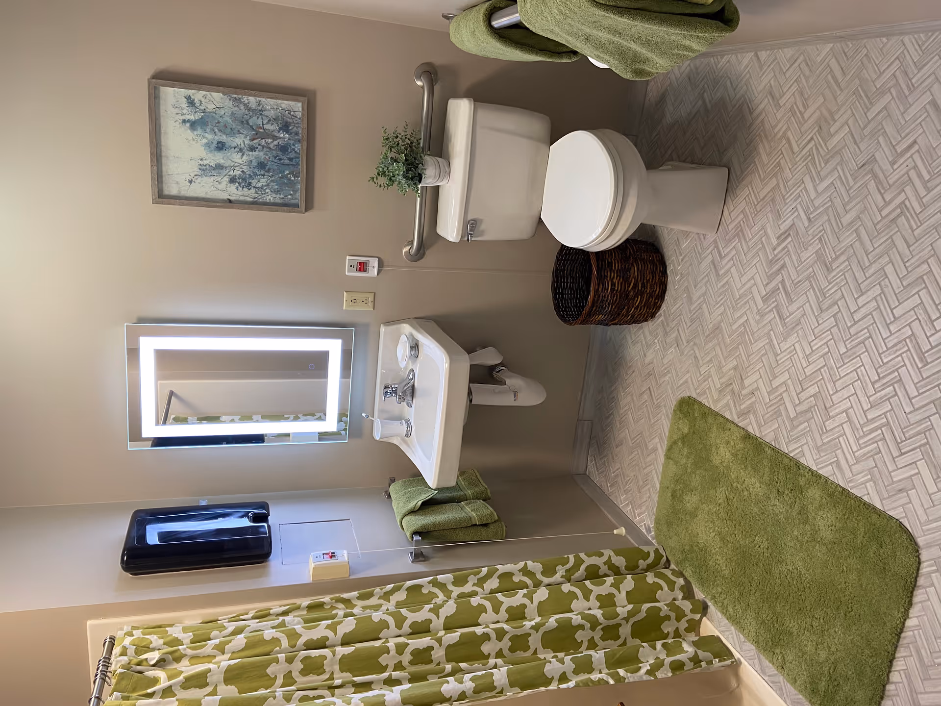 White bathroom with sink, toilet, mirror, green towels, shower curtain, and green rug.