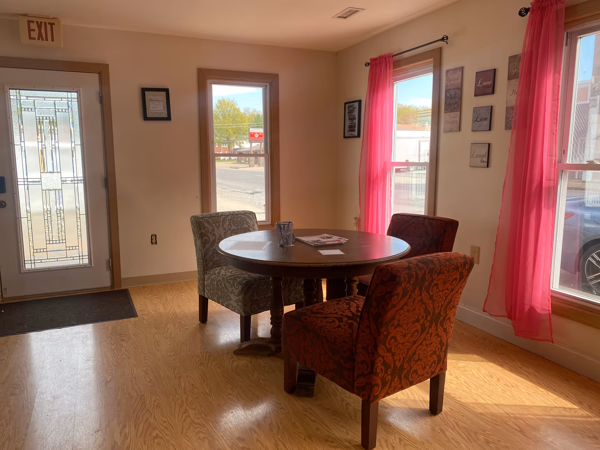 Interior dining area with a round wooden table and pink-curtained windows.
