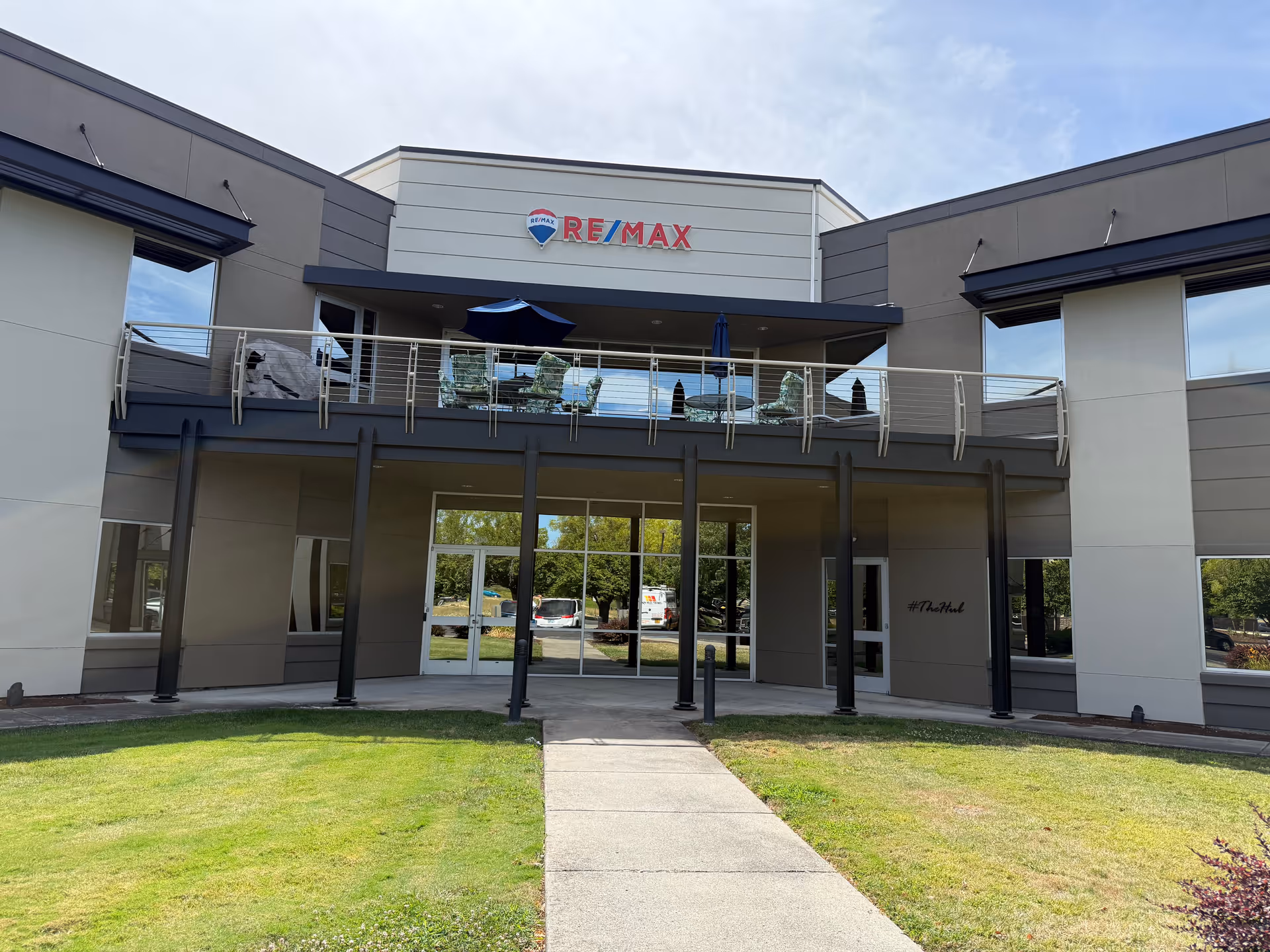 Front view of a modern senior living facility with RE/MAX sign, glass entrance, balcony.