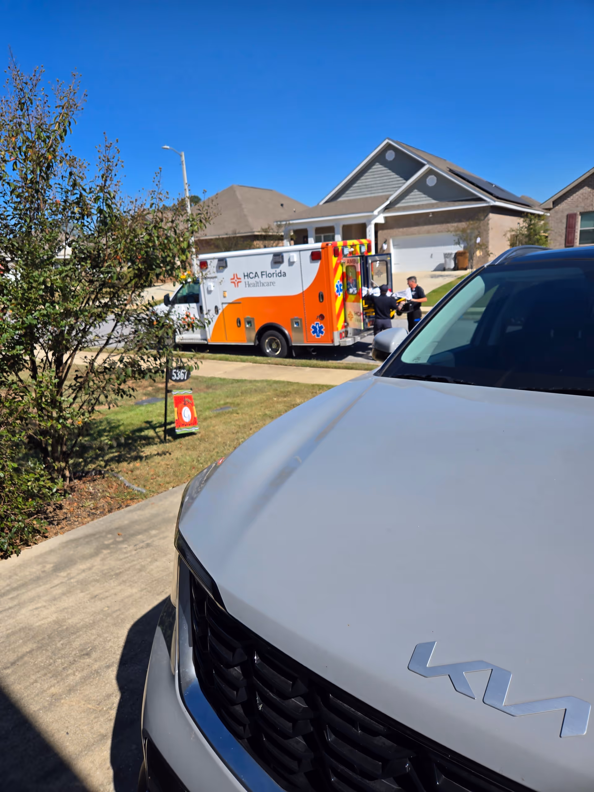 Ambulance from HCA Florida Healthcare parked in front of a house, with a gray SUV nearby.