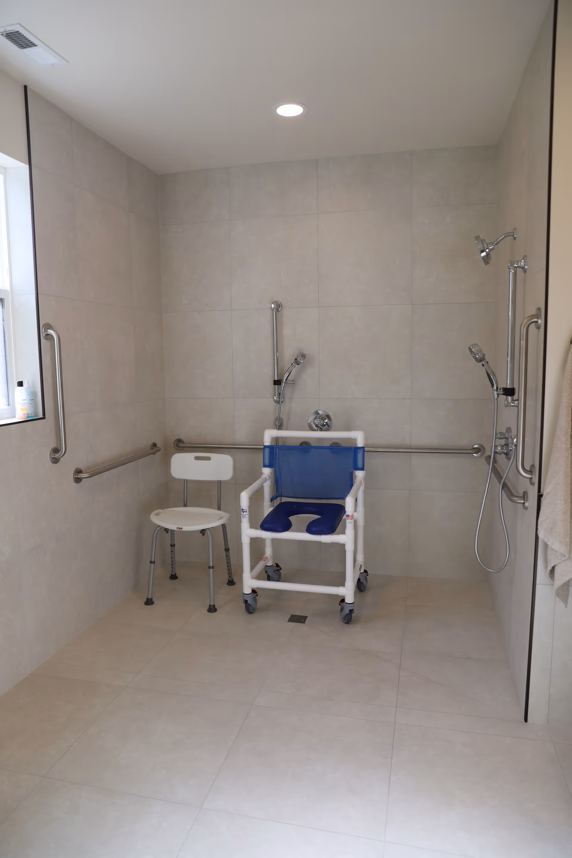 Accessible bathroom with grab bars, a blue shower chair, and a small stool.