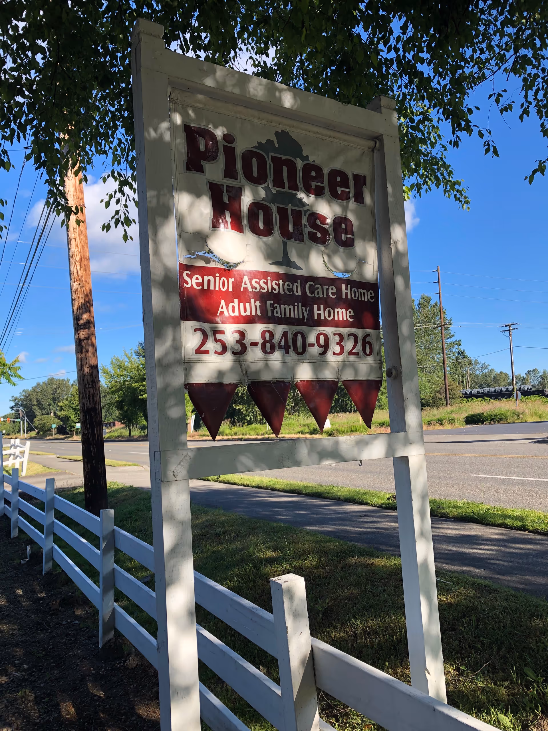 Outdoor sign for Pioneer House Senior Assisted Care near a white fence and road.
