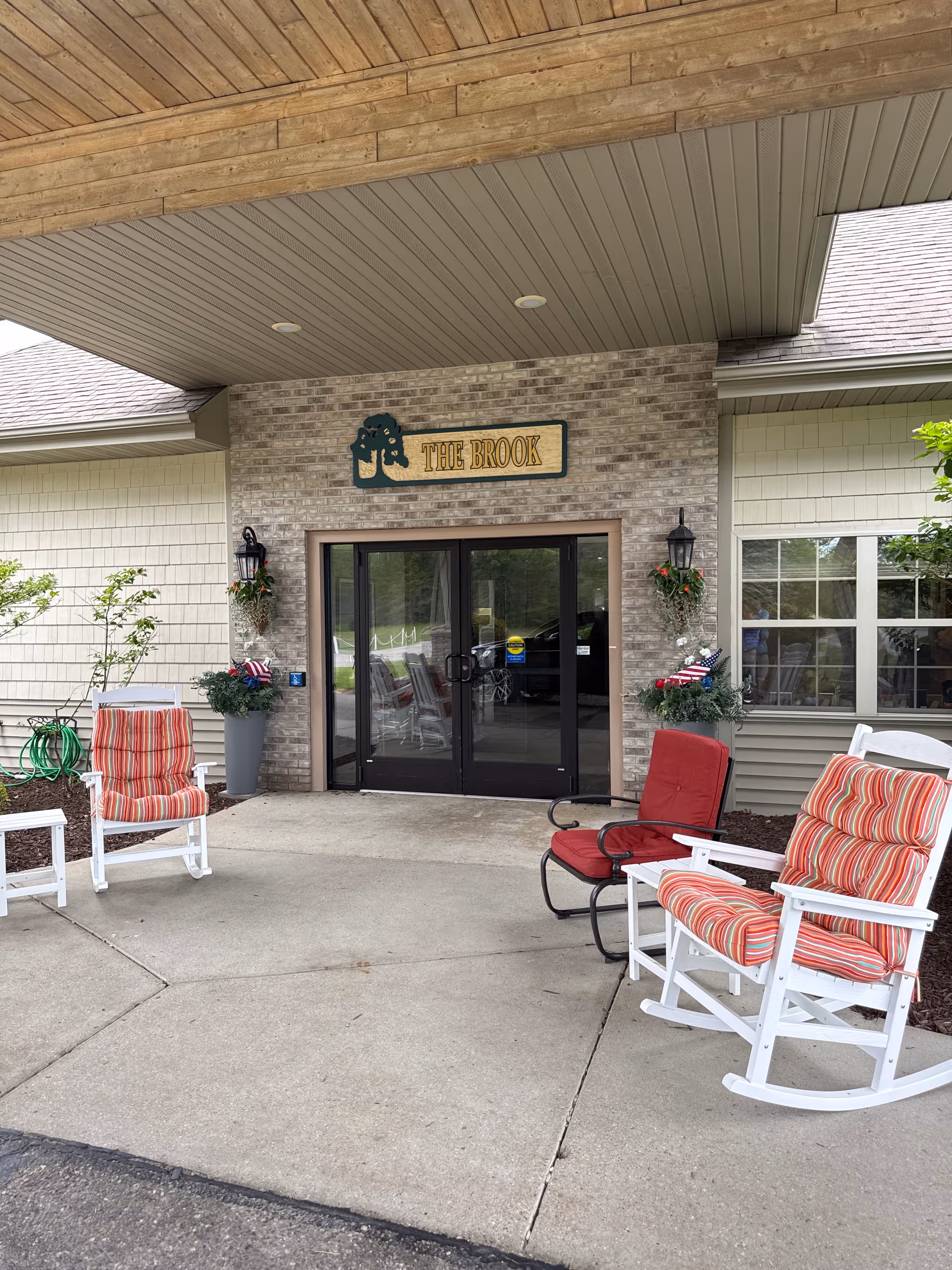 Entrance to The Brook of Roscommon with brick facade, glass doors, and outdoor seating.