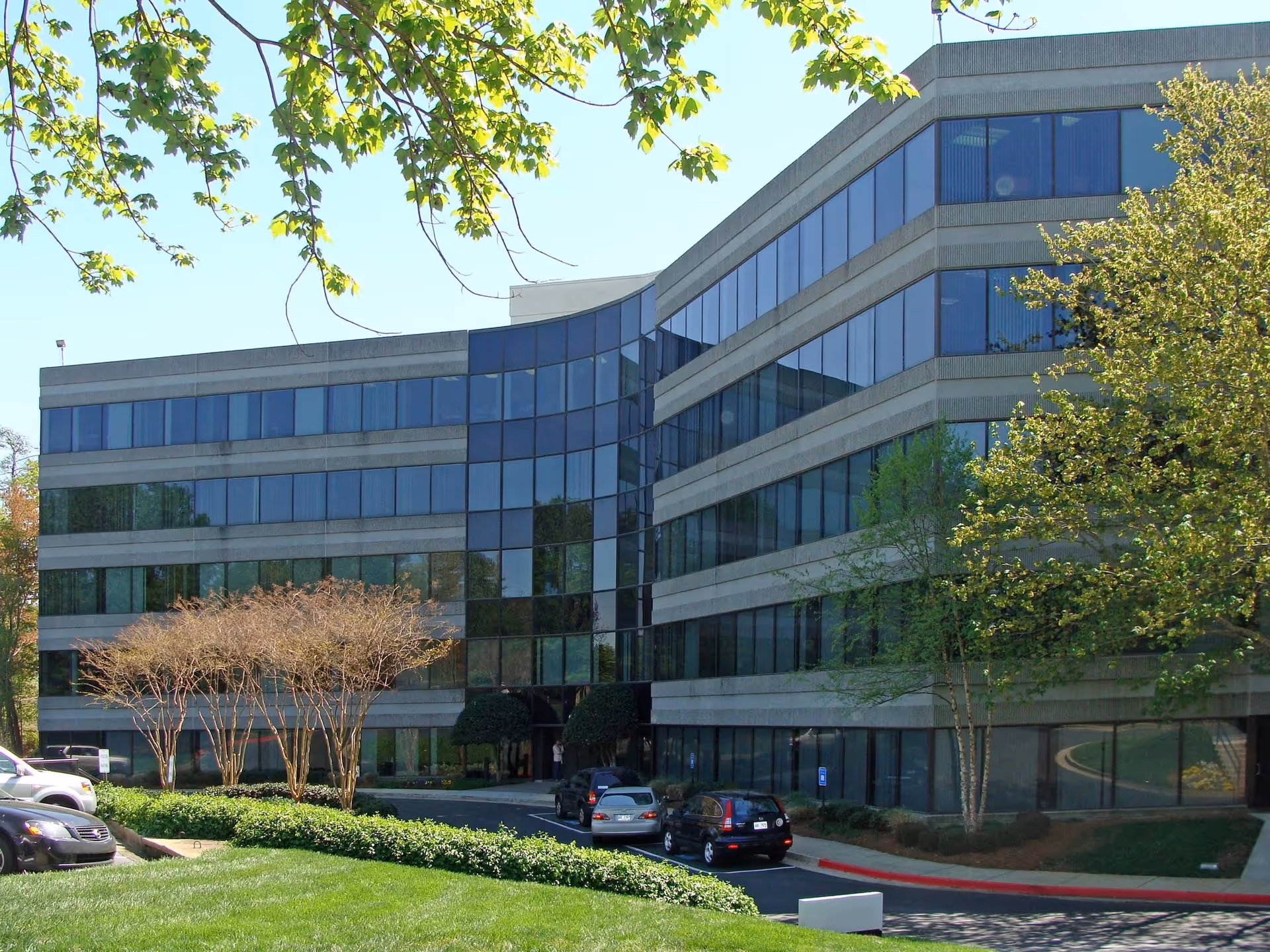 Atlas ProCare building with a glass facade, landscaped surroundings, and parked cars.