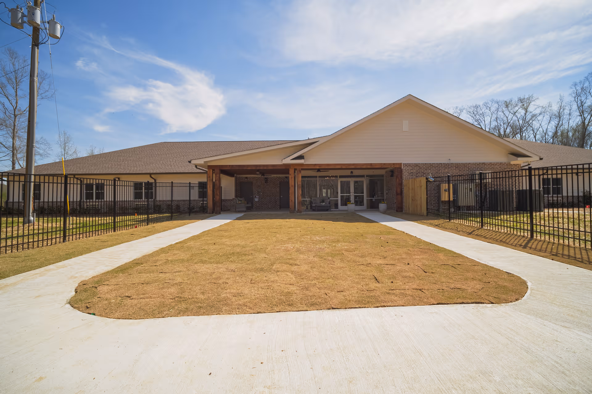 Single-story brick facility with a covered entrance, fenced perimeter, and curved concrete driveway.
