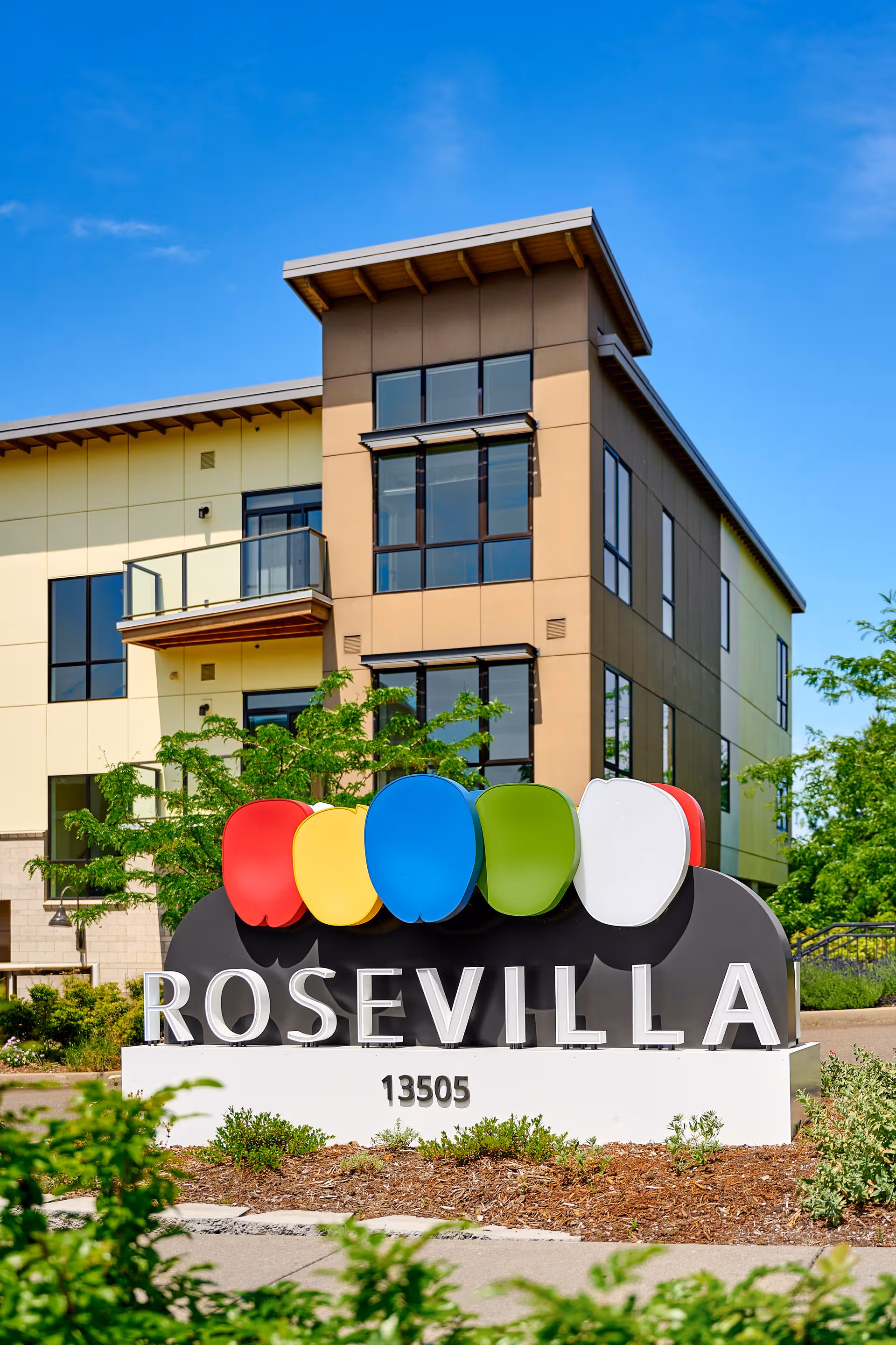 Modern multi-story senior living building with a colorful RoseVilla sign at the entrance.