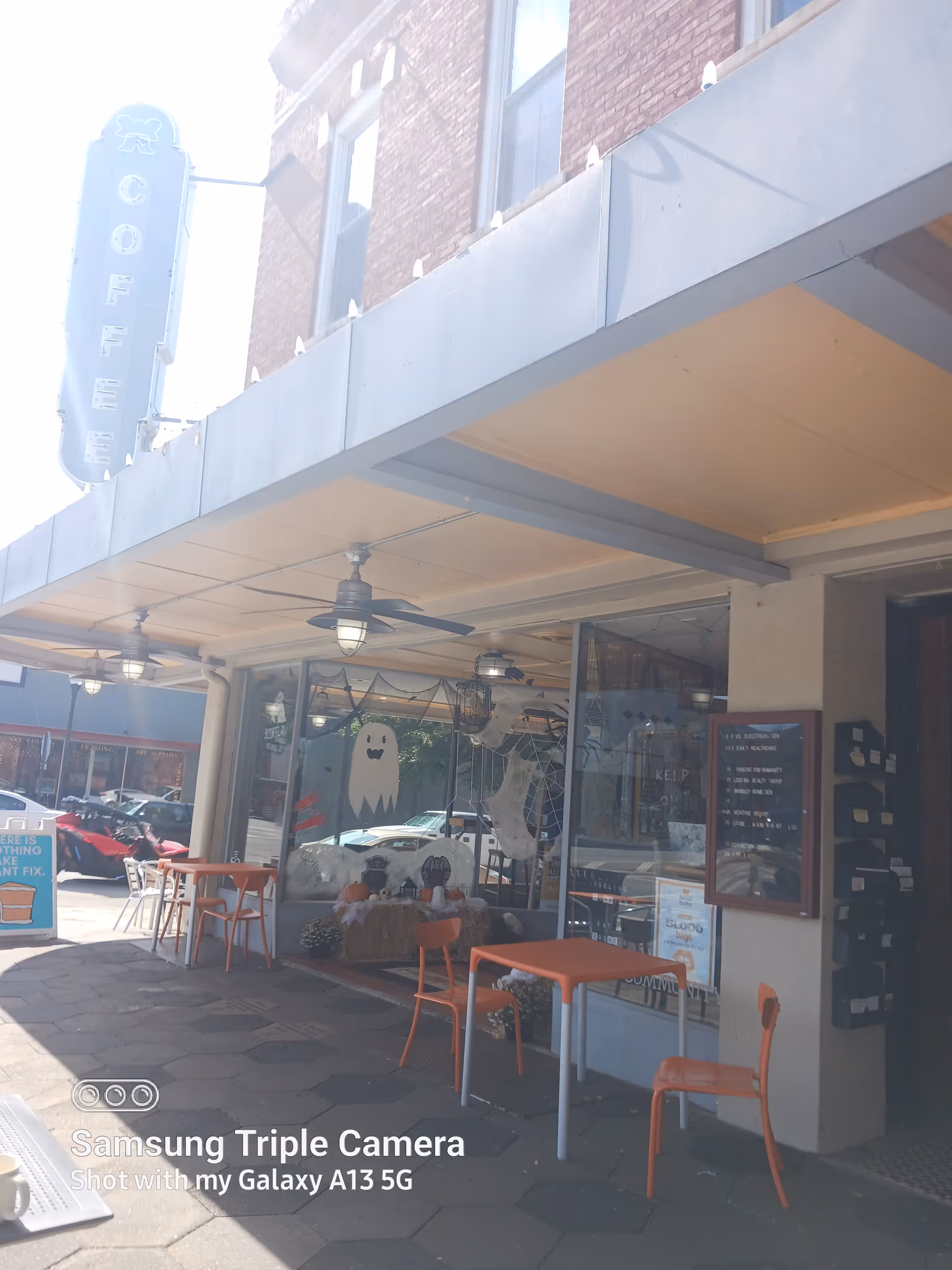 Outdoor cafe seating along a storefront under a canopy with Halloween decorations.