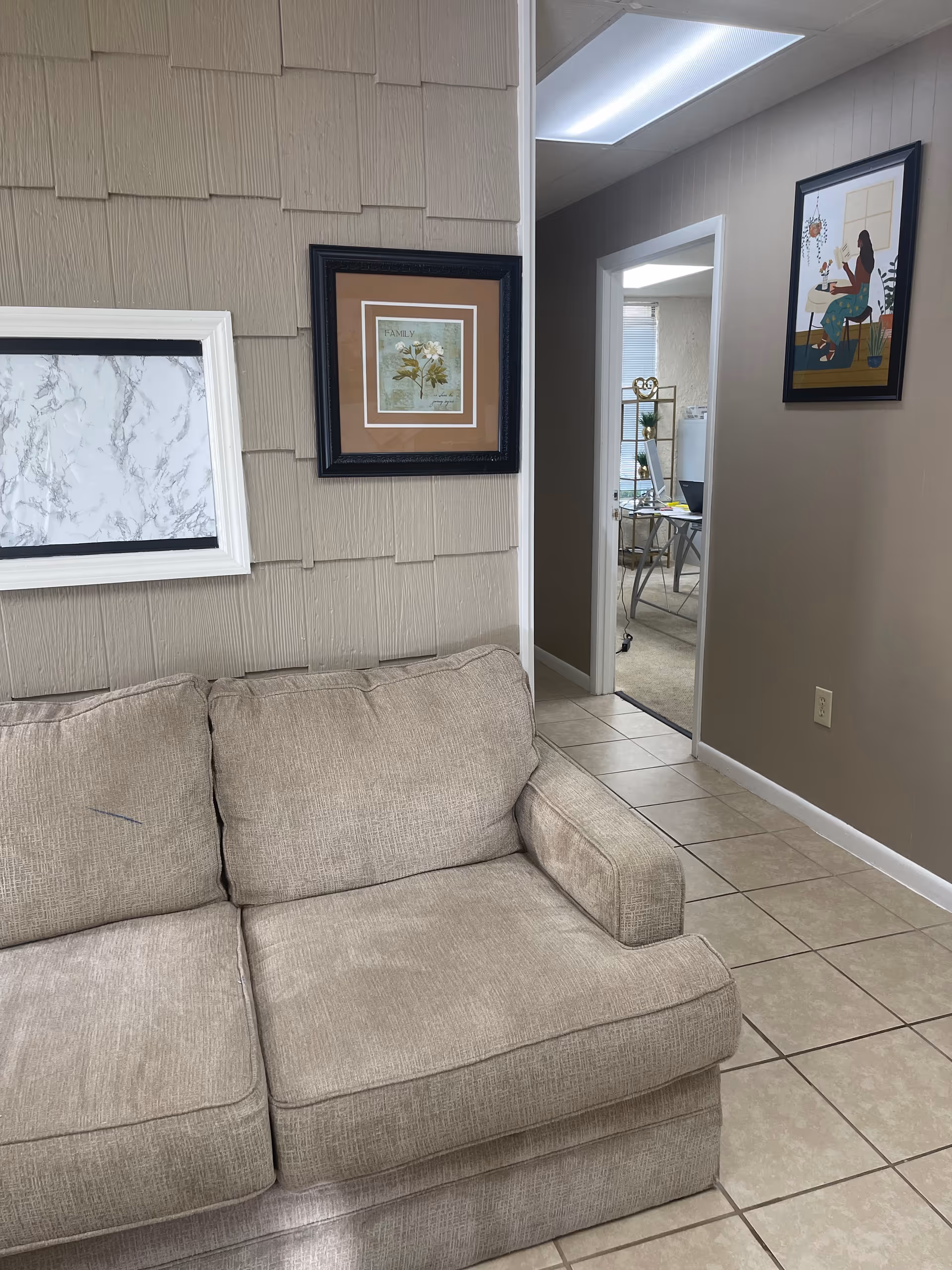 Beige sofa in a tiled living room with wall art and an open doorway.