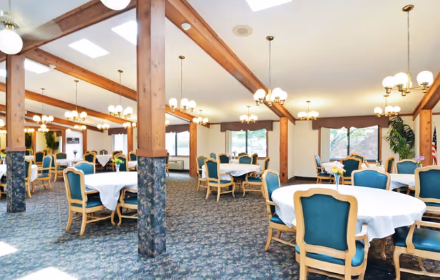 Spacious dining room with round tables, teal chairs, and wood-beamed ceiling.
