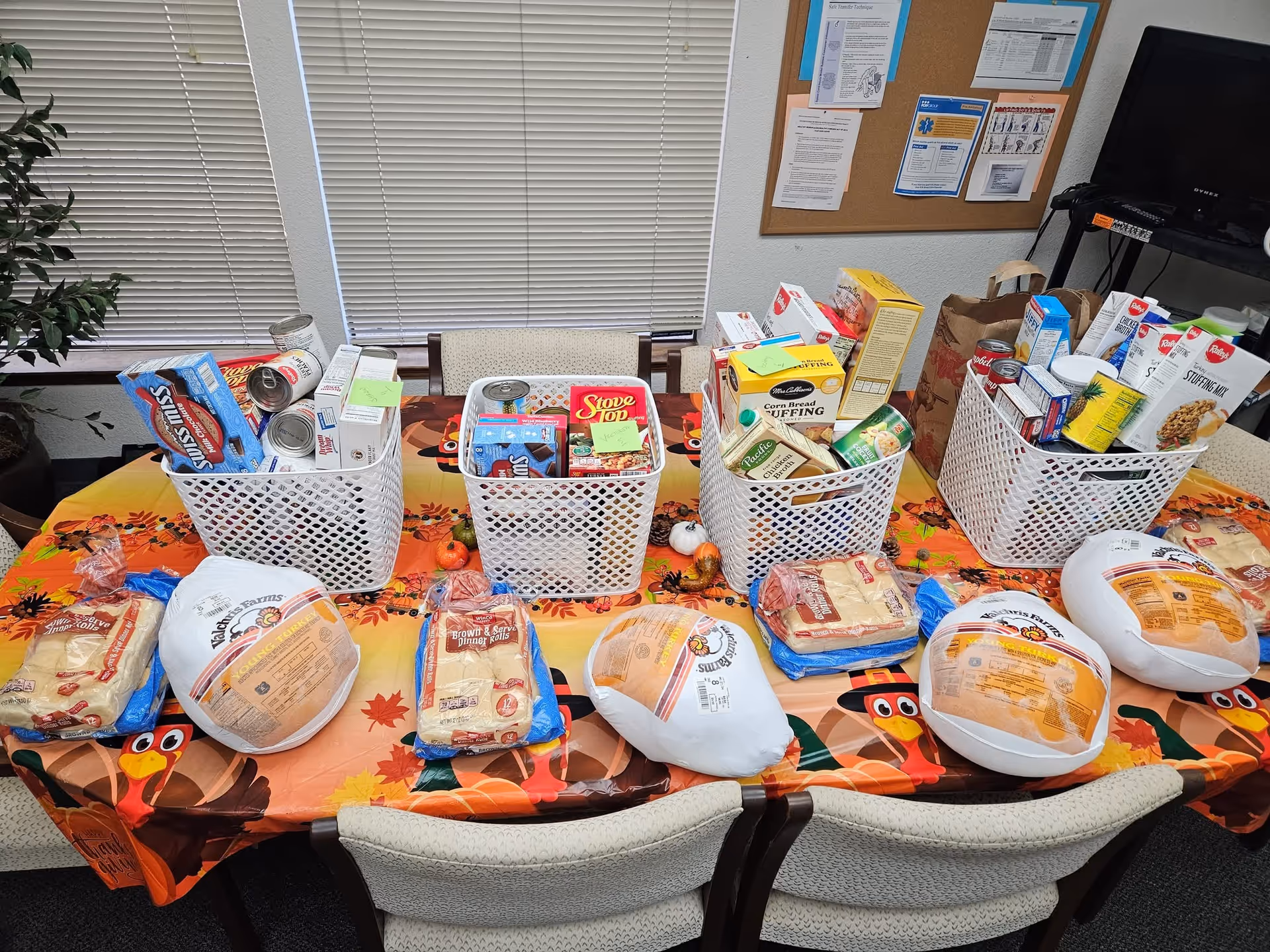 Indoor room with four white baskets filled with groceries on a fall-themed table.