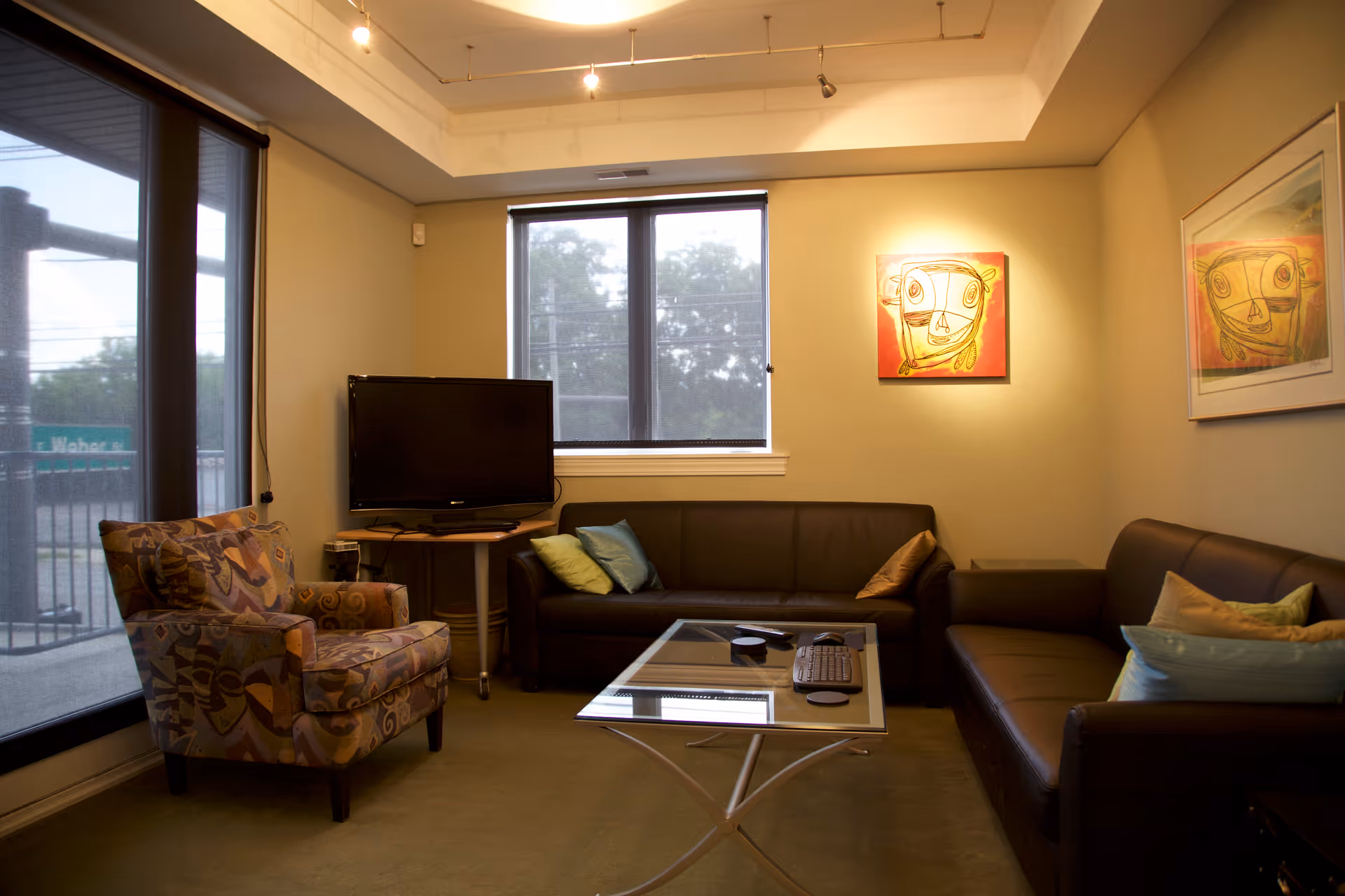 Cozy living room lounge with leather sofas, glass coffee table, TV, and wall art.