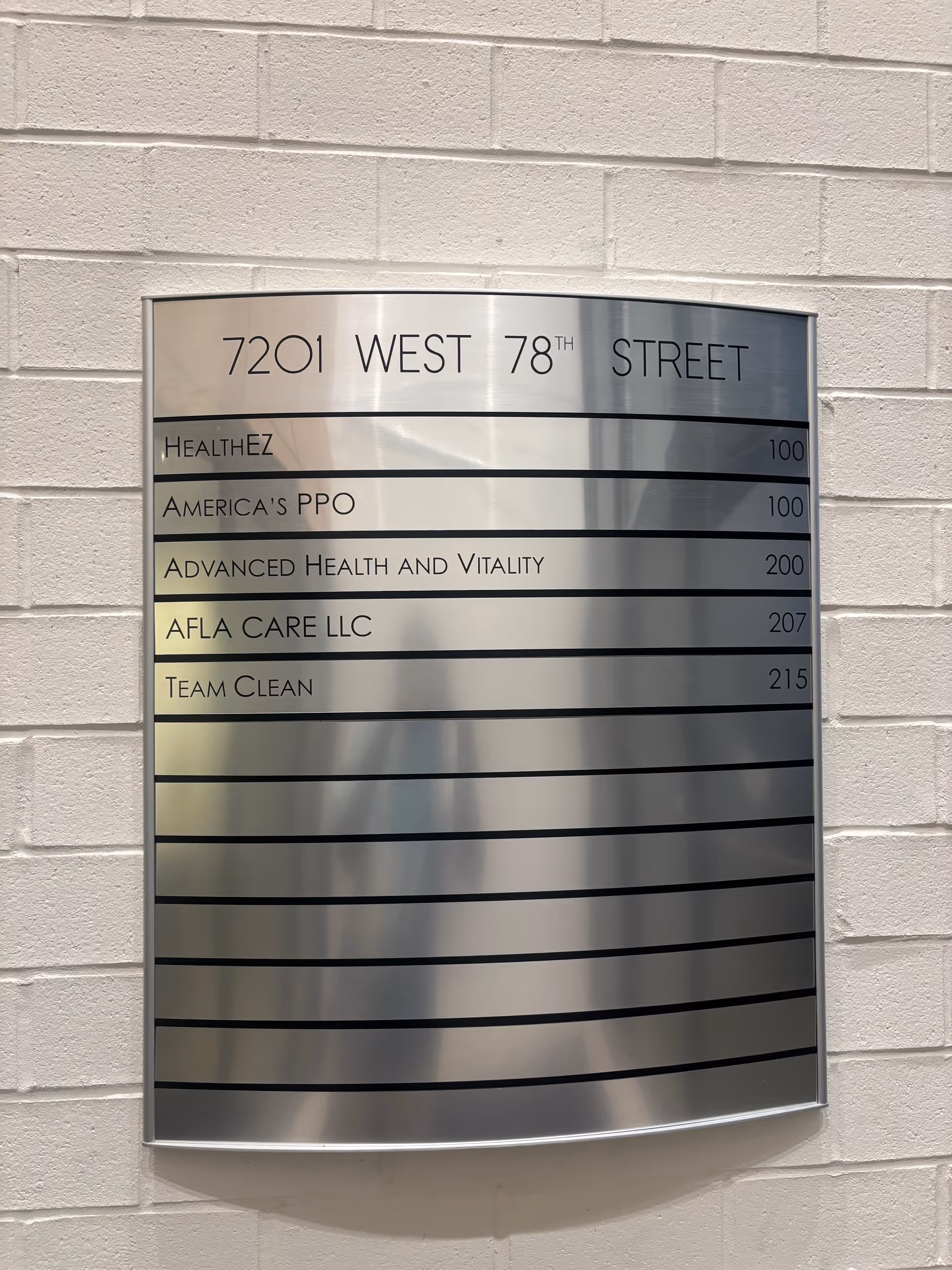 Metal directory plaque mounted on a white brick wall listing company names and address.