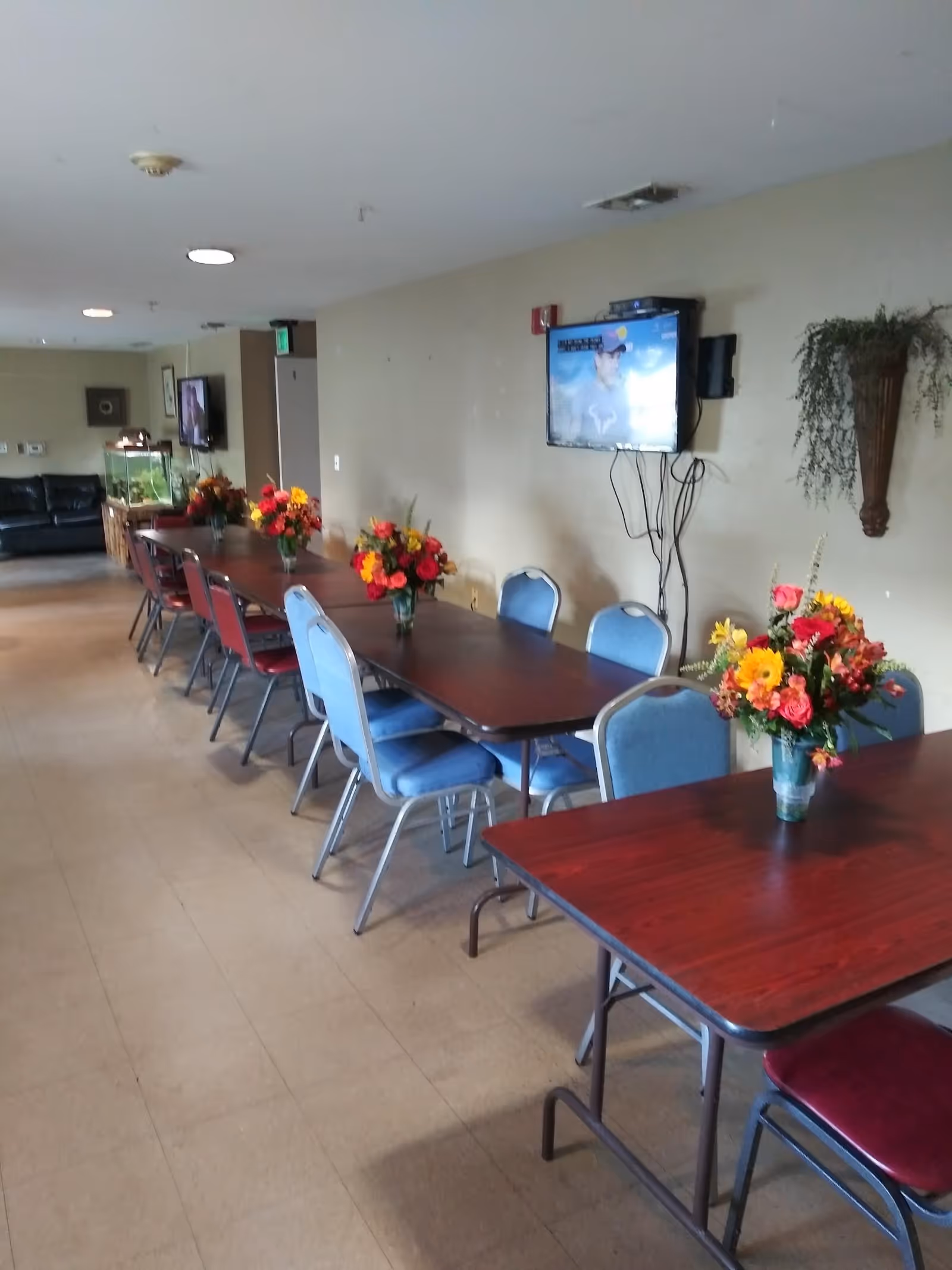Long dining tables with flower centerpieces and a wall mounted TV in a communal dining area.