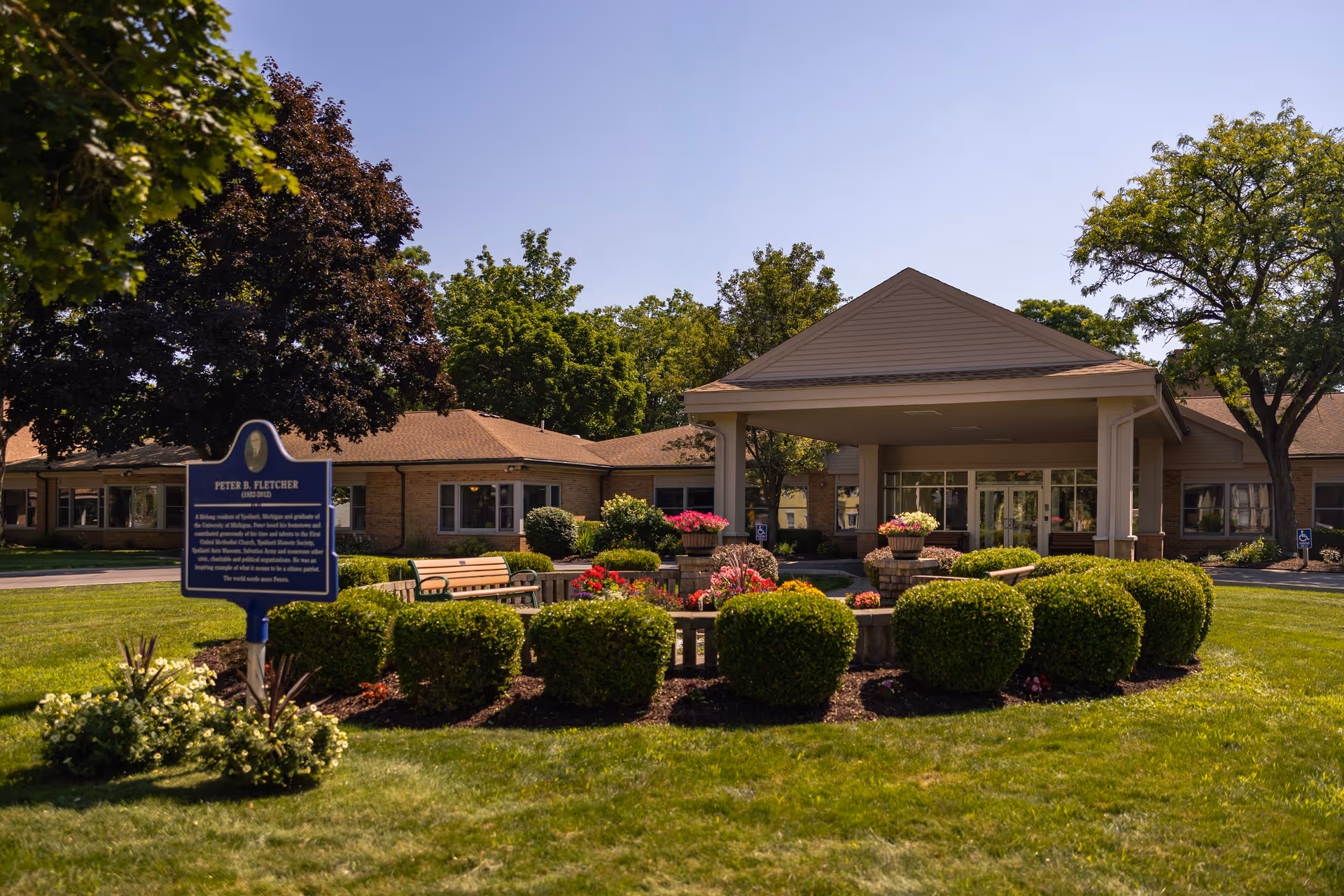 Exterior view of Gilbert Residence entrance with manicured shrubs and benches.