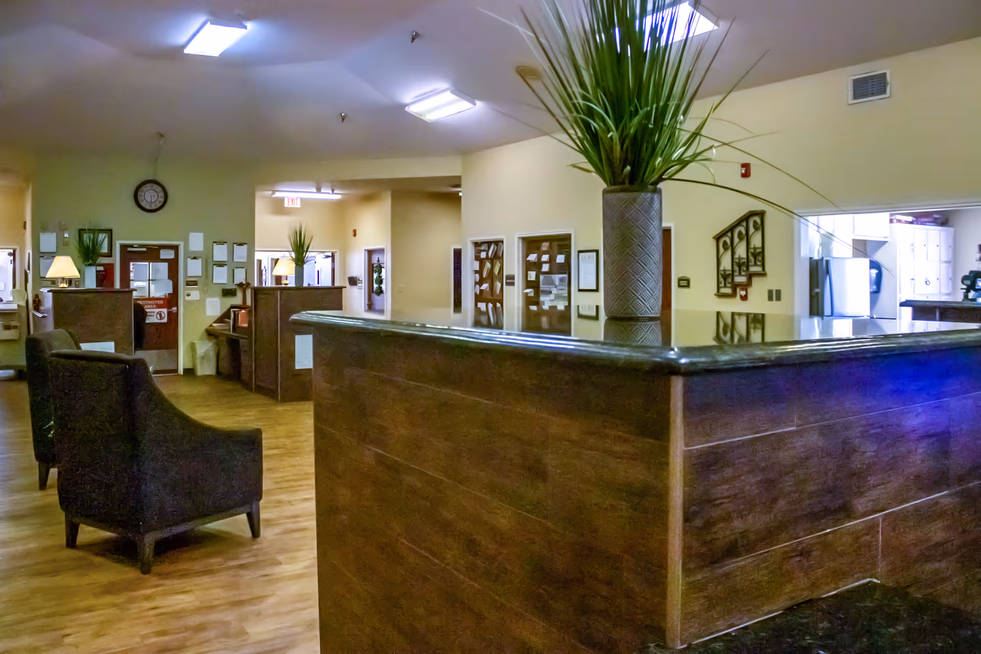 A facility lobby with a dark wood reception desk, seating, and potted plant.