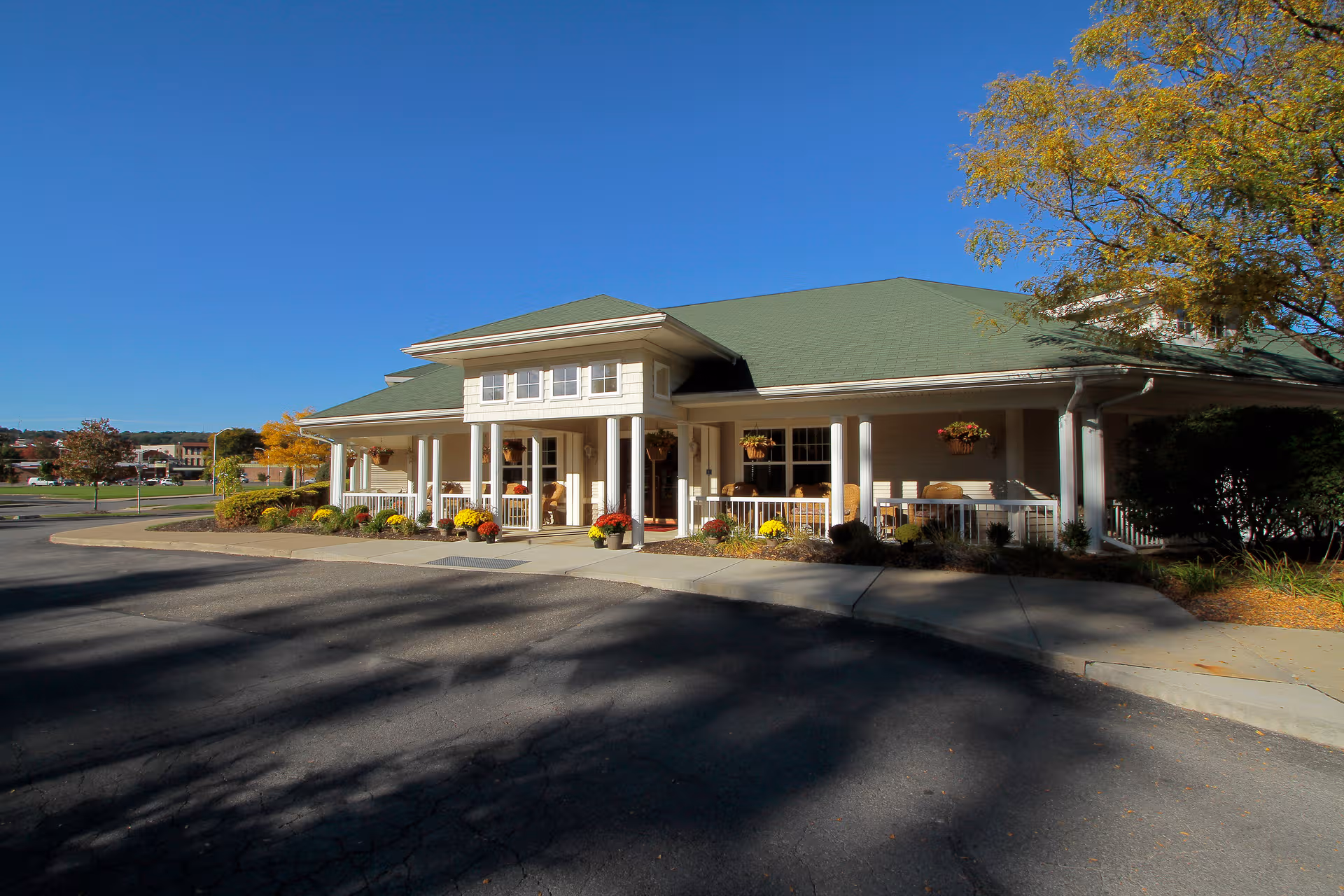 Front entrance of a Senior Living facility with white pillars, flowers, and a green roof.