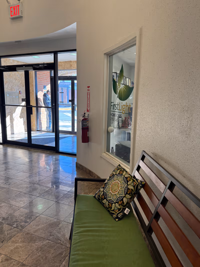 Interior hallway with a wooden bench, green cushion, and a window advertising FirstLight Home Care.