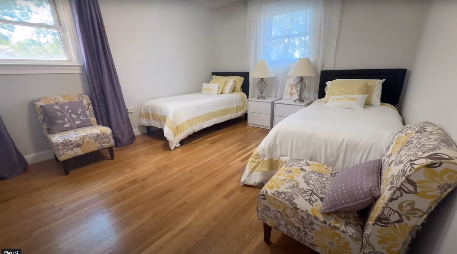 Two twin beds with matching bedding, nightstands, lamps, and seating in a bright bedroom.