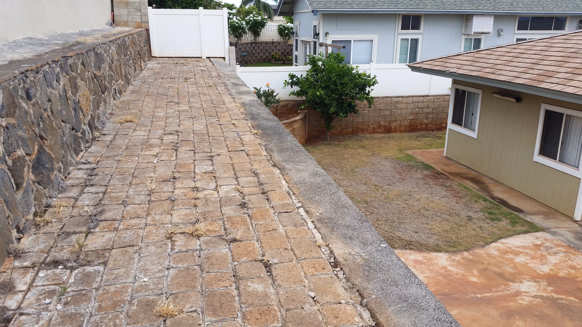 Outdoor brick walkway beside a stone wall and a beige facility building.