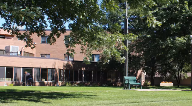 Exterior of Majestic Pines senior living facility with lawn, trees, and a bench.