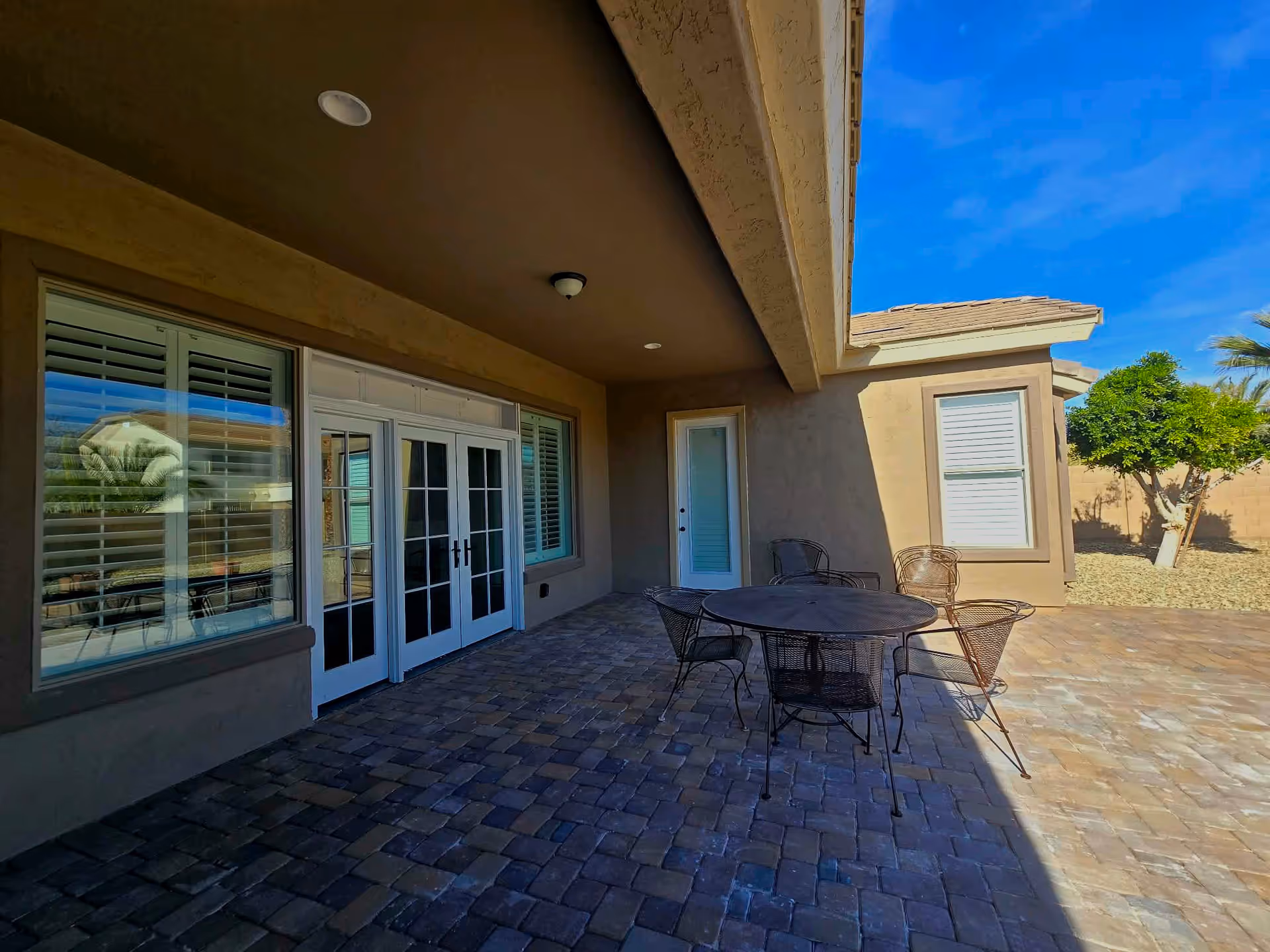Covered patio with metal table and chairs outside a beige building under a blue sky.