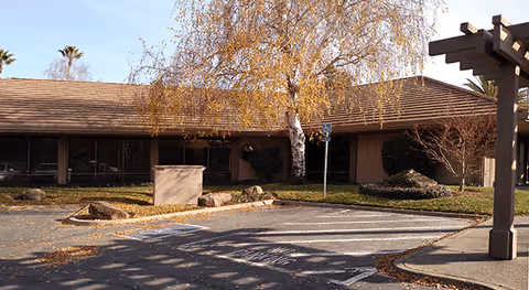 Single-story Caregivers of Land Park LLC exterior with parking lot and autumn trees.