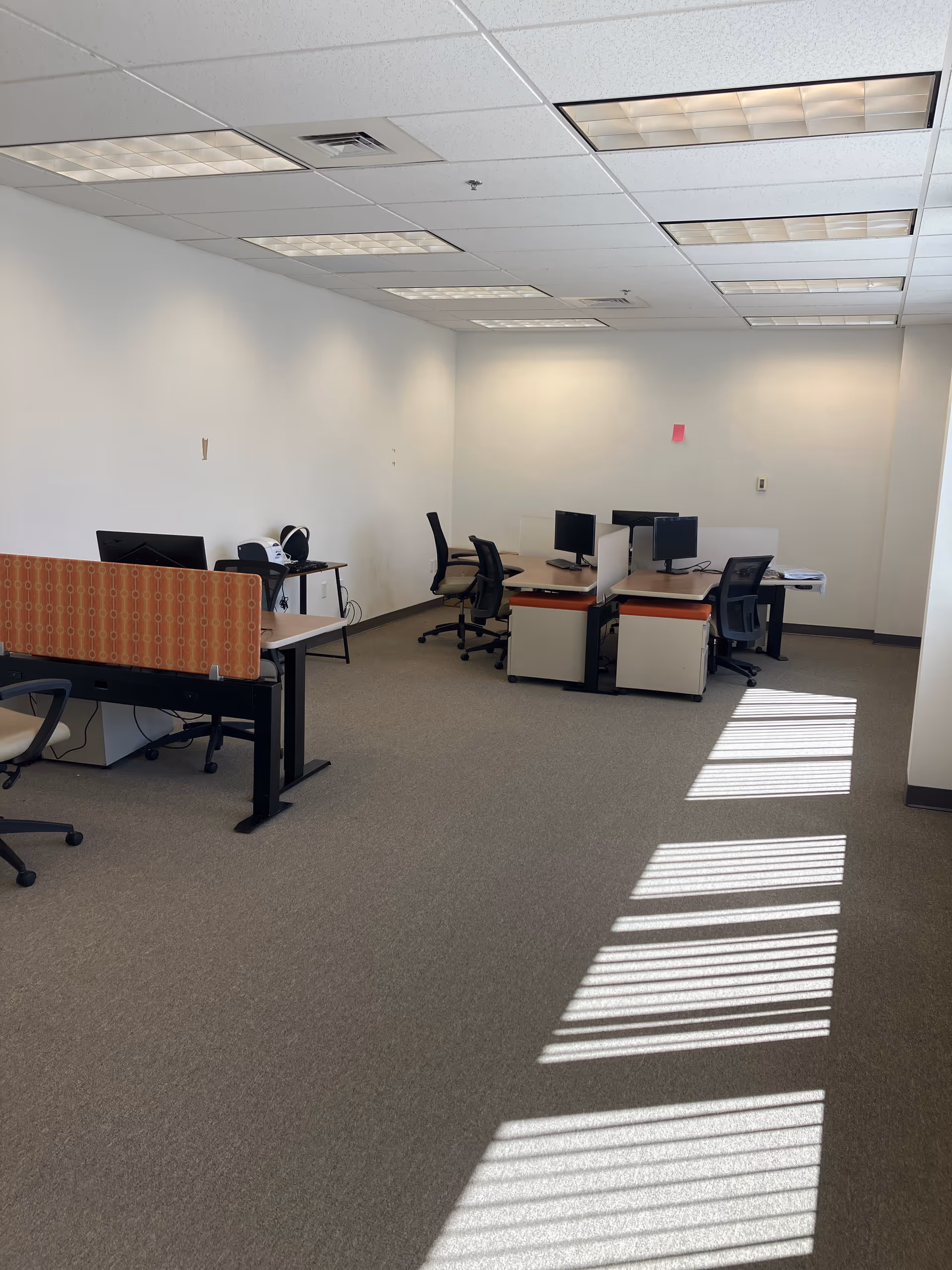 An empty office workspace with desks, computers, and chairs in a bright room.
