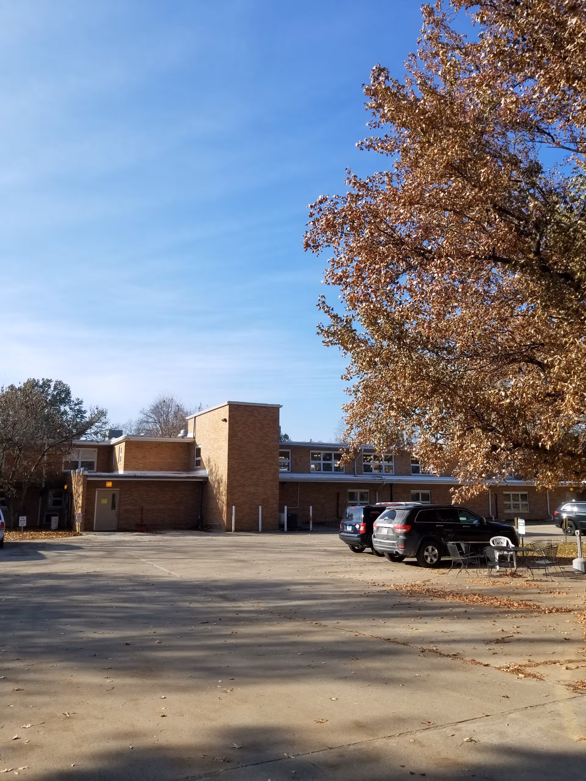 Exterior view of Rushville Nursing and Rehab Center with parked cars and autumn trees.
