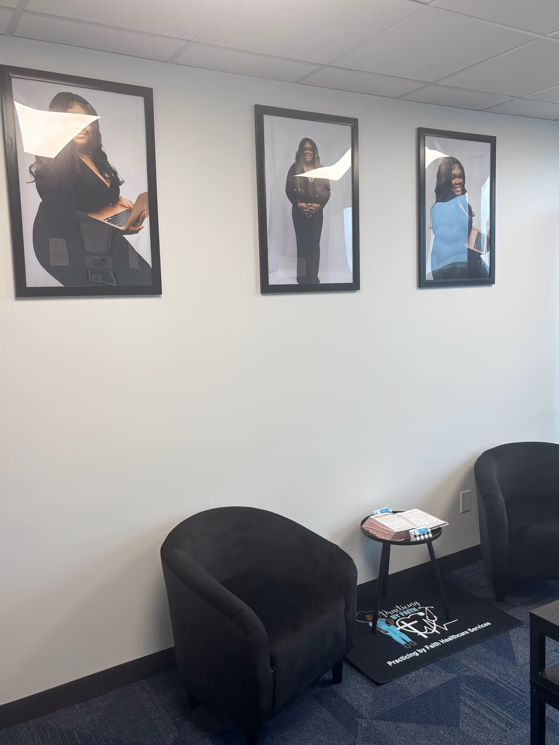 Small interior seating area with two black chairs, a round table, and wall portraits.