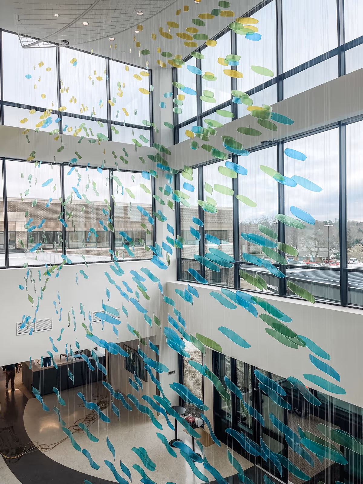 Bright interior atrium with large glass walls and hanging blue-green leaf art.