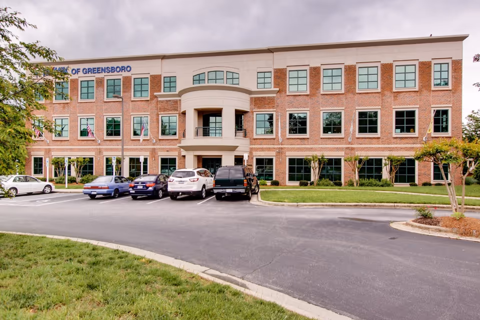 Three-story brick senior living facility with a curved entrance and a parking lot in front.