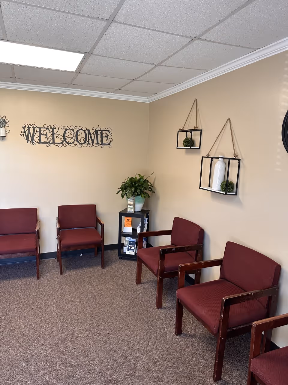 Interior waiting area with burgundy chairs, beige walls, and a 'Welcome' sign.