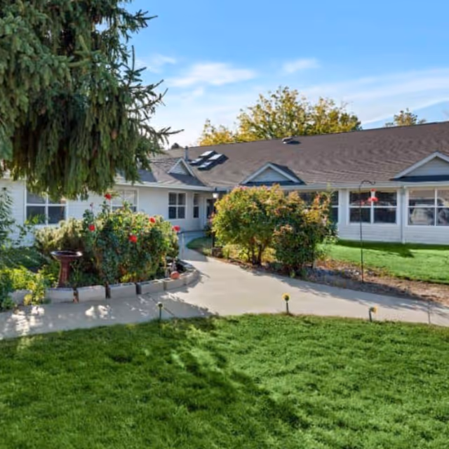 Exterior view of Three Rivers Place senior living building with walkway and landscaped garden.