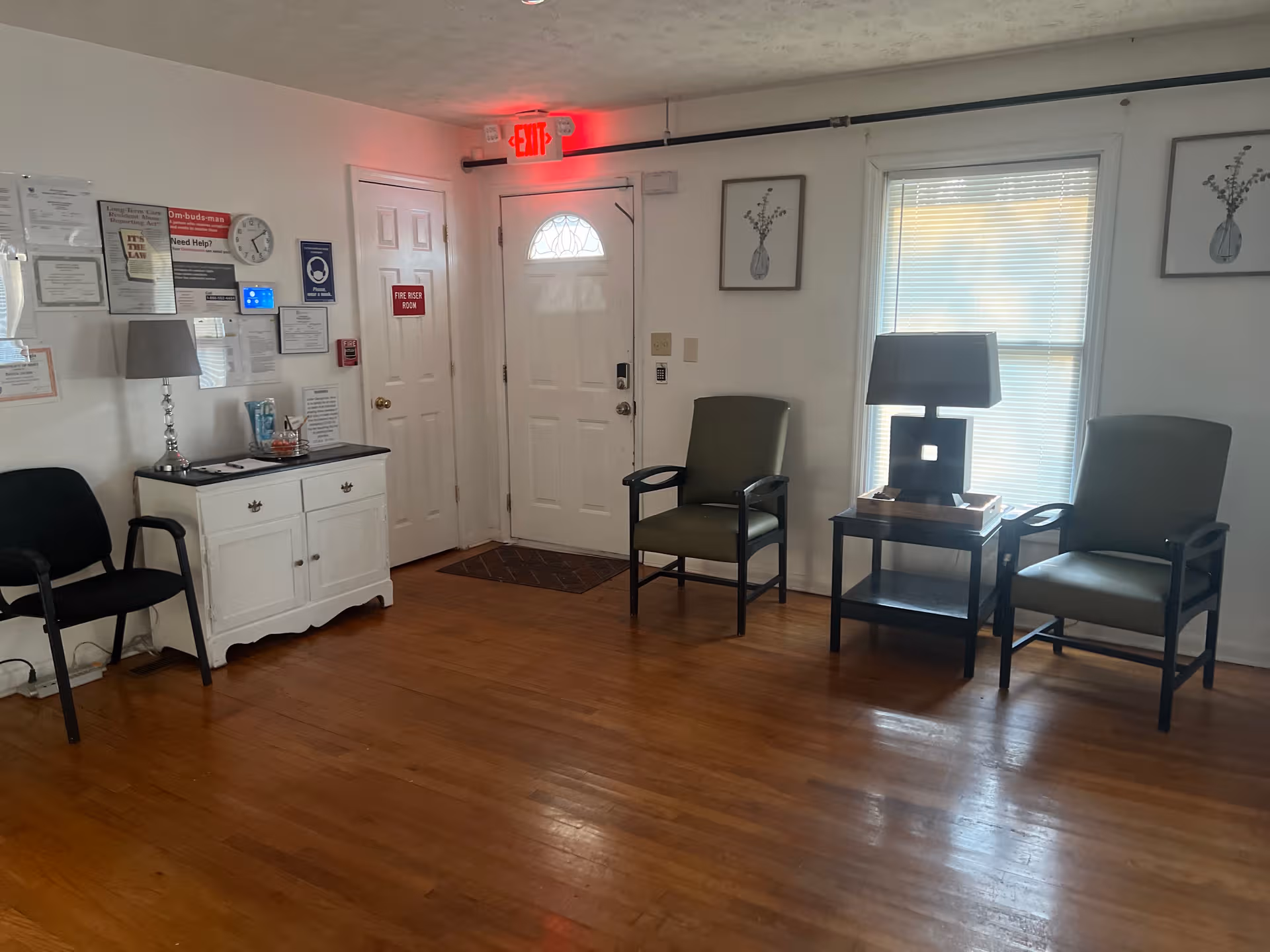 Empty waiting area with chairs, a small table, and wall decor in a hallway.