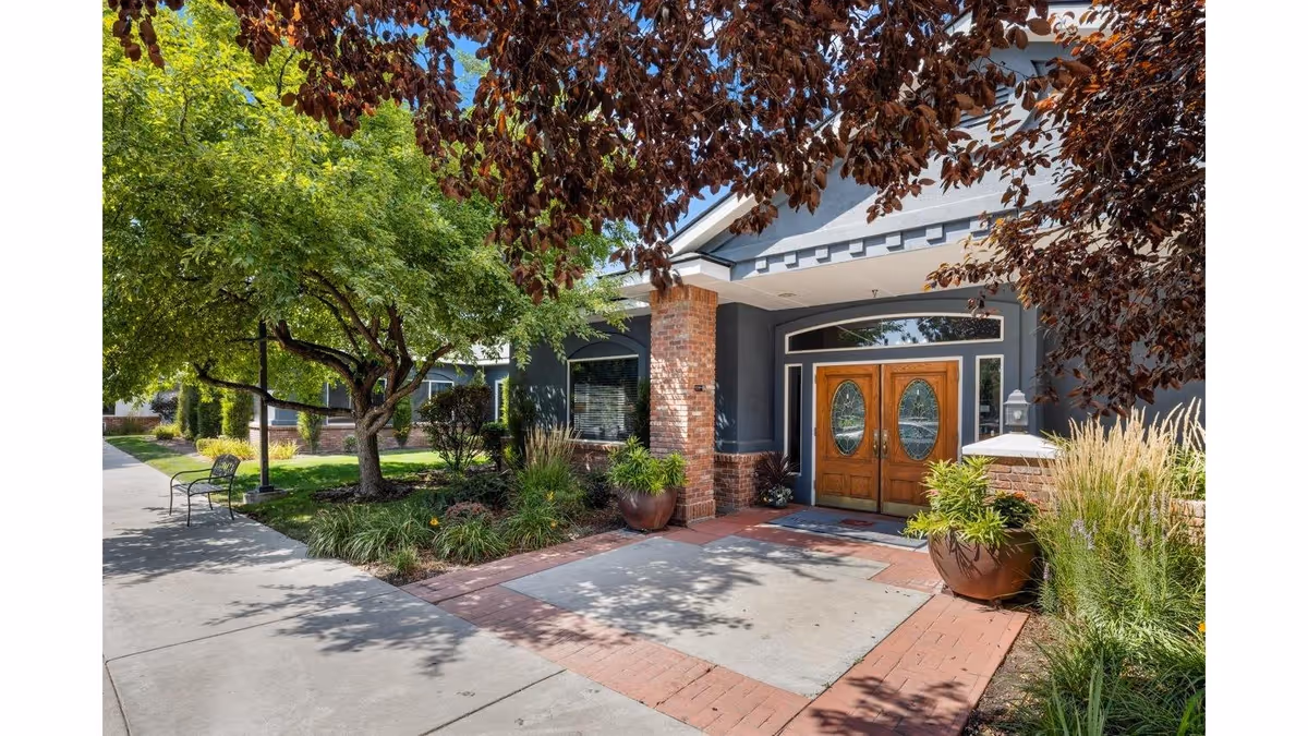 Front entrance of a senior living facility with wooden double doors and landscaped surroundings.