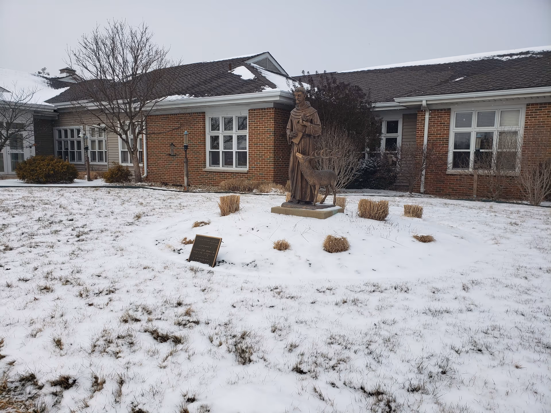 Brick hospice building with a statue and deer sculpture in a snowy front yard.