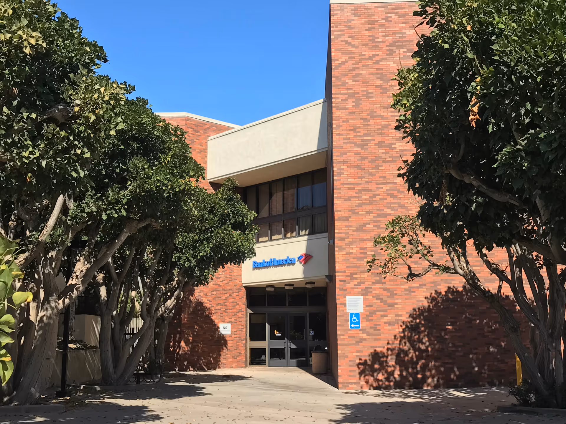 A brick building entrance is framed by trees with glass doors and an accessible sign.