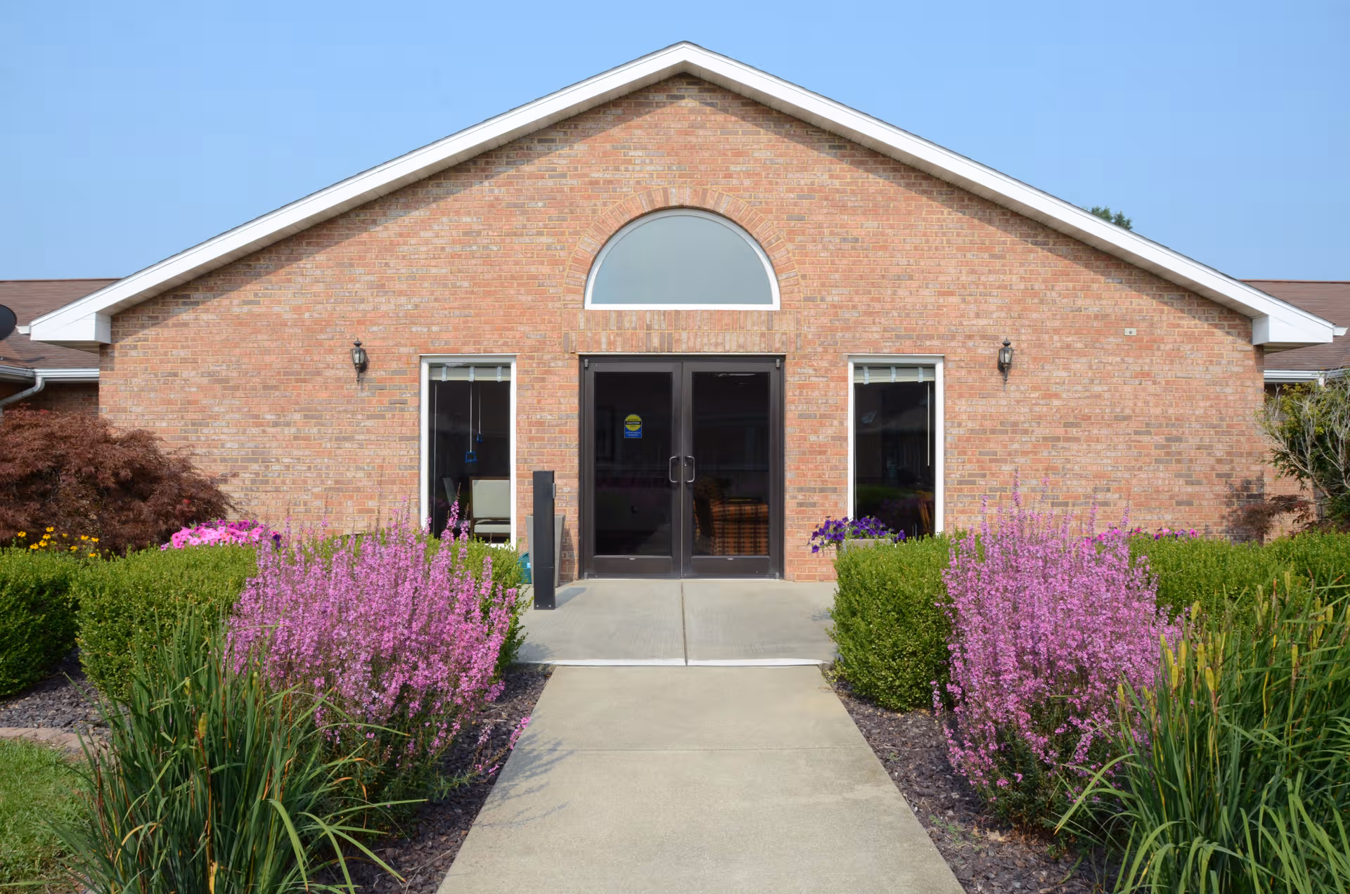 Taylorville Estates front entrance: brick building, glass doors, arched window, flowering landscaping.