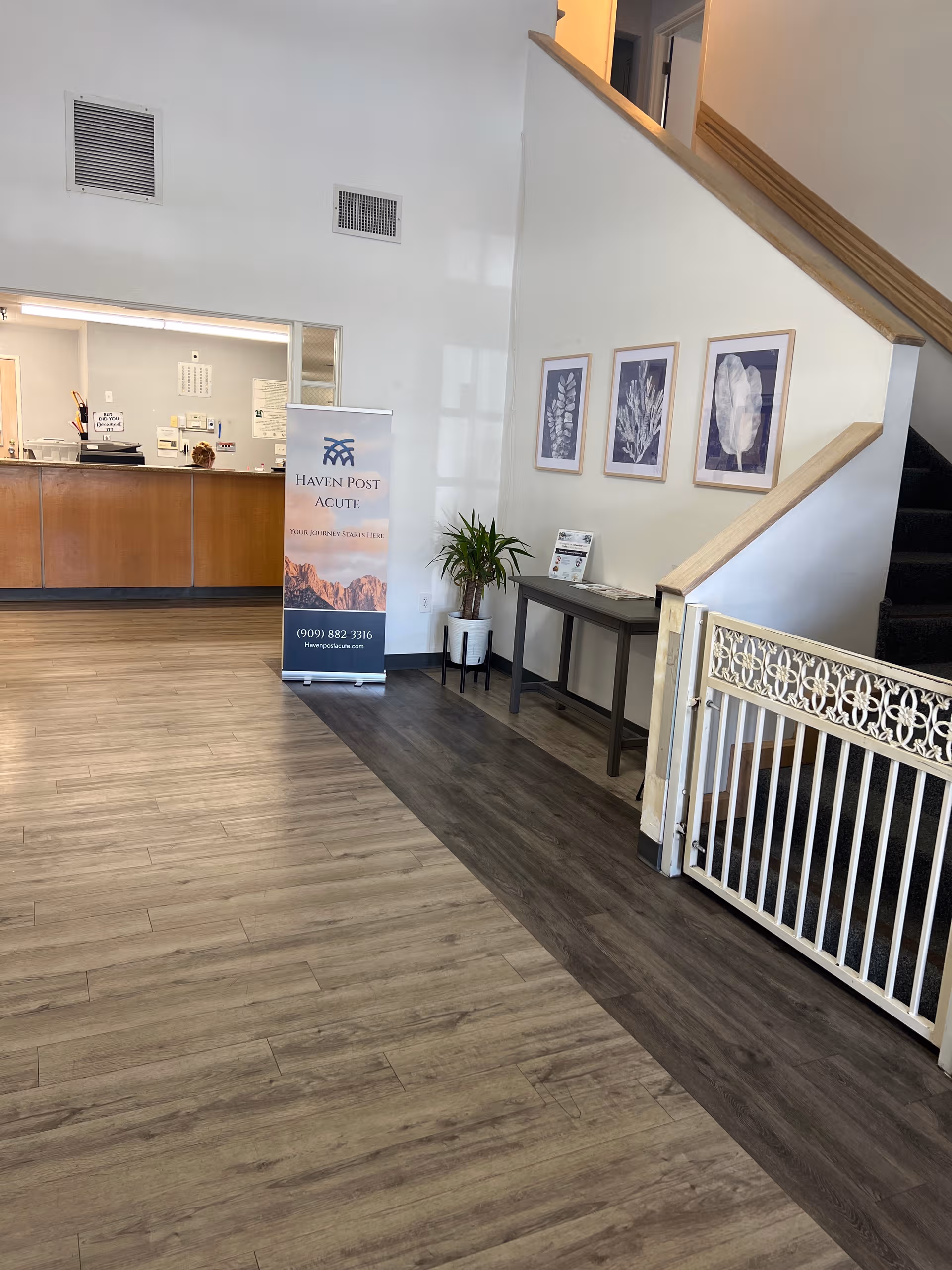 Lobby area with a reception desk, banner, plant, staircase, and framed wall art.