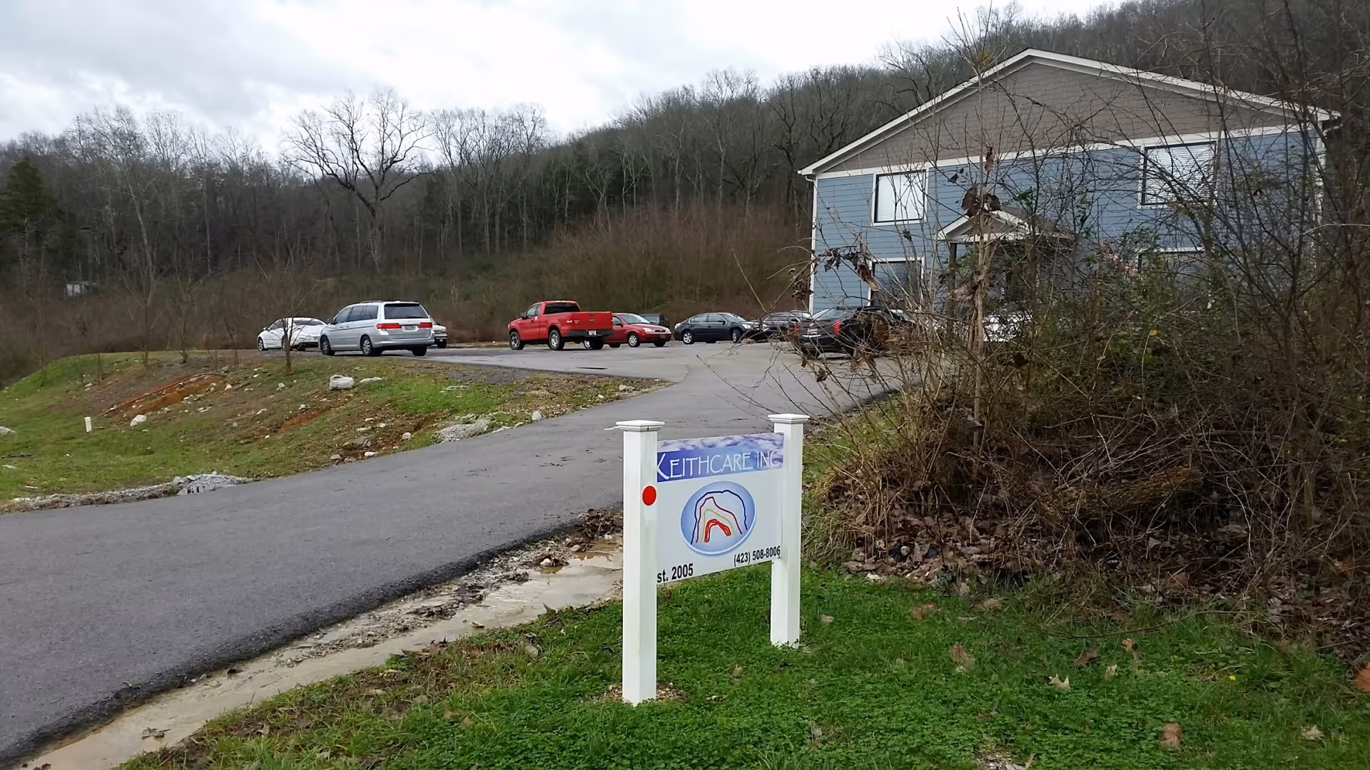 Keithcare Inc sign at the entrance of a blue facility with parked cars.