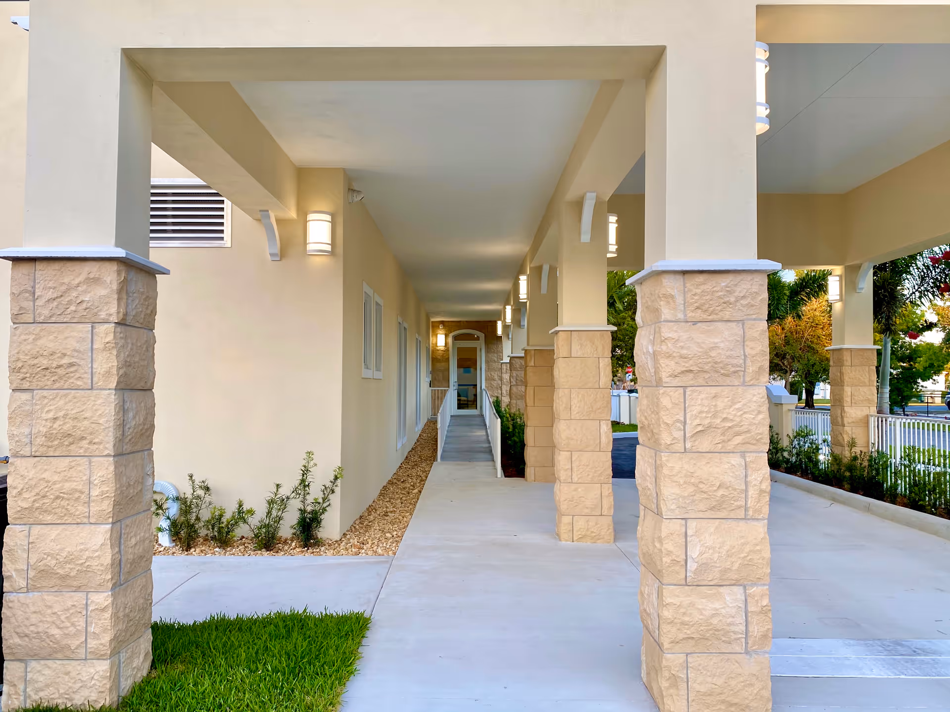 Covered exterior walkway with stone columns and beige walls at MiCasa Senior Living.