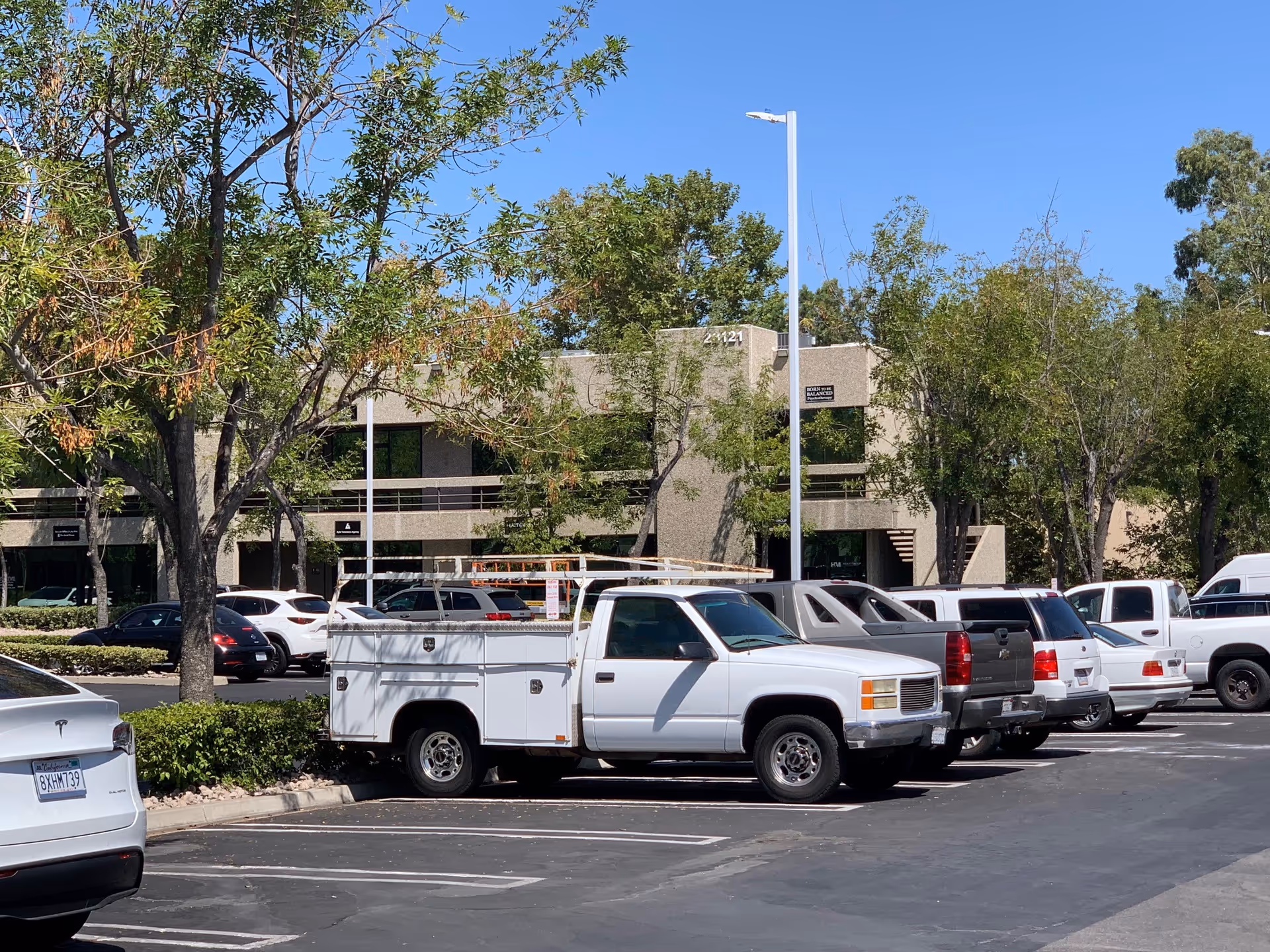 Parking lot in front of a beige senior living building with trees and several parked vehicles.
