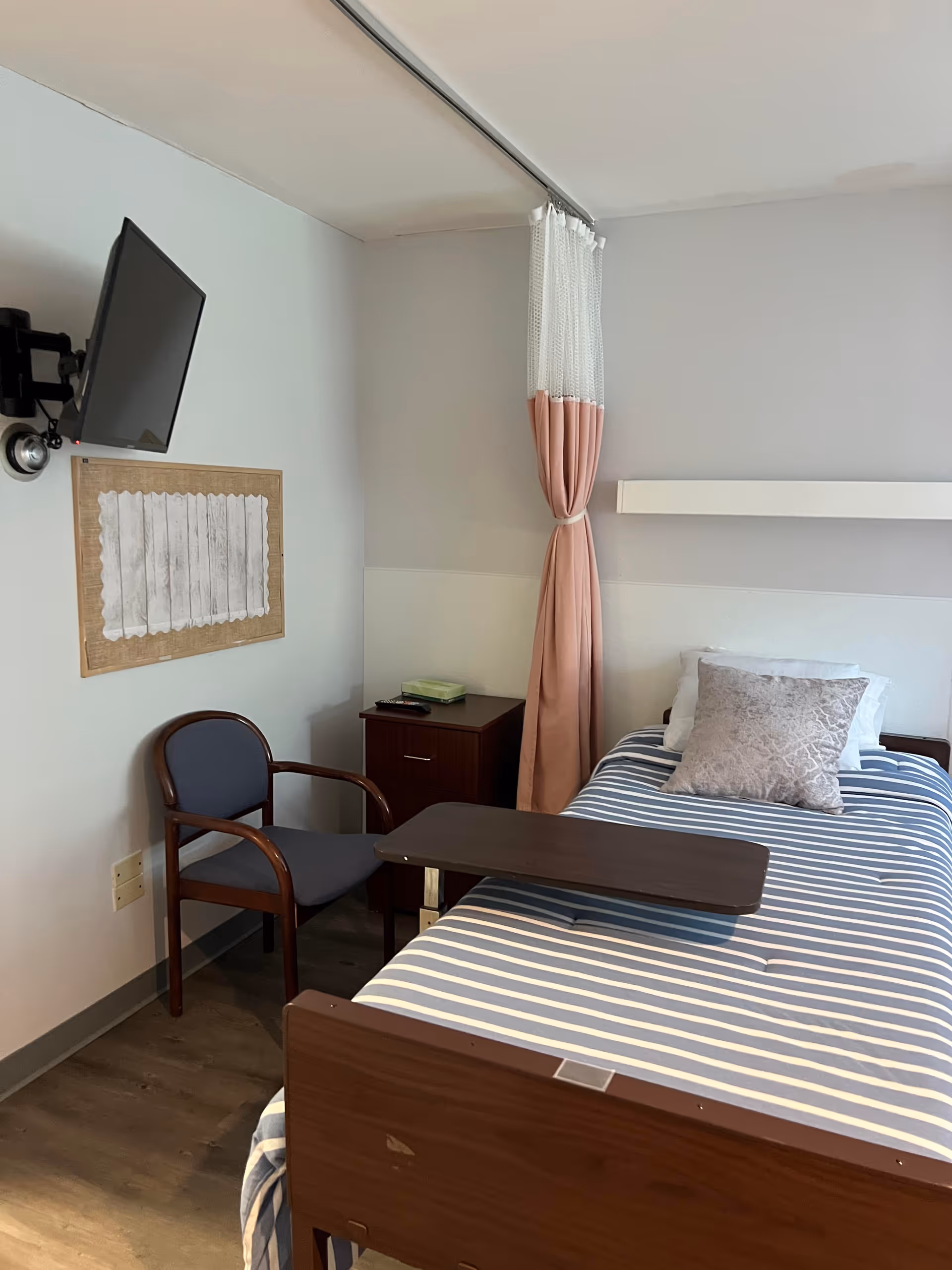 A single hospital-style bedroom with striped bed, curtain, chair, and TV.