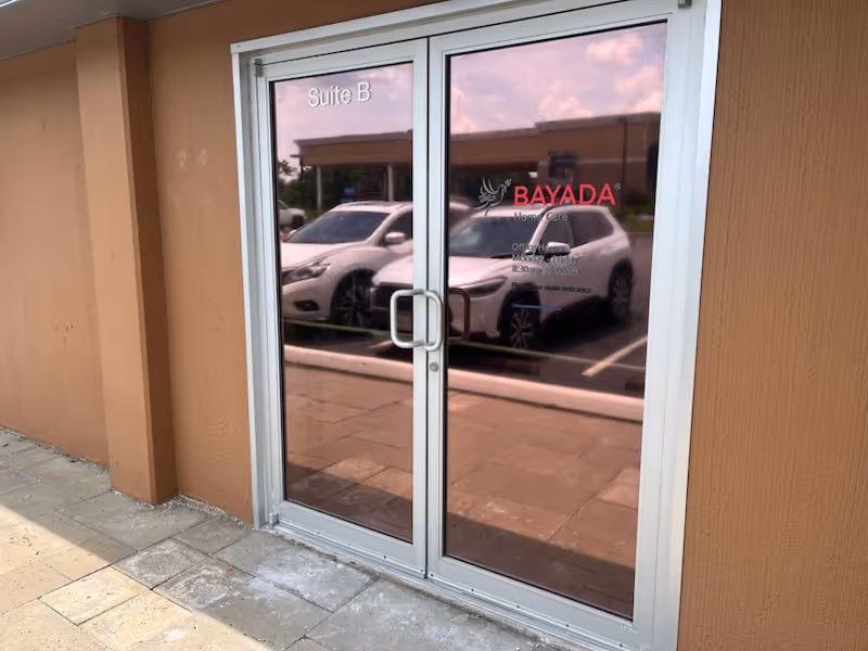 Glass double doors marked Suite B with reflections of parked cars outside the BAYADA facility
