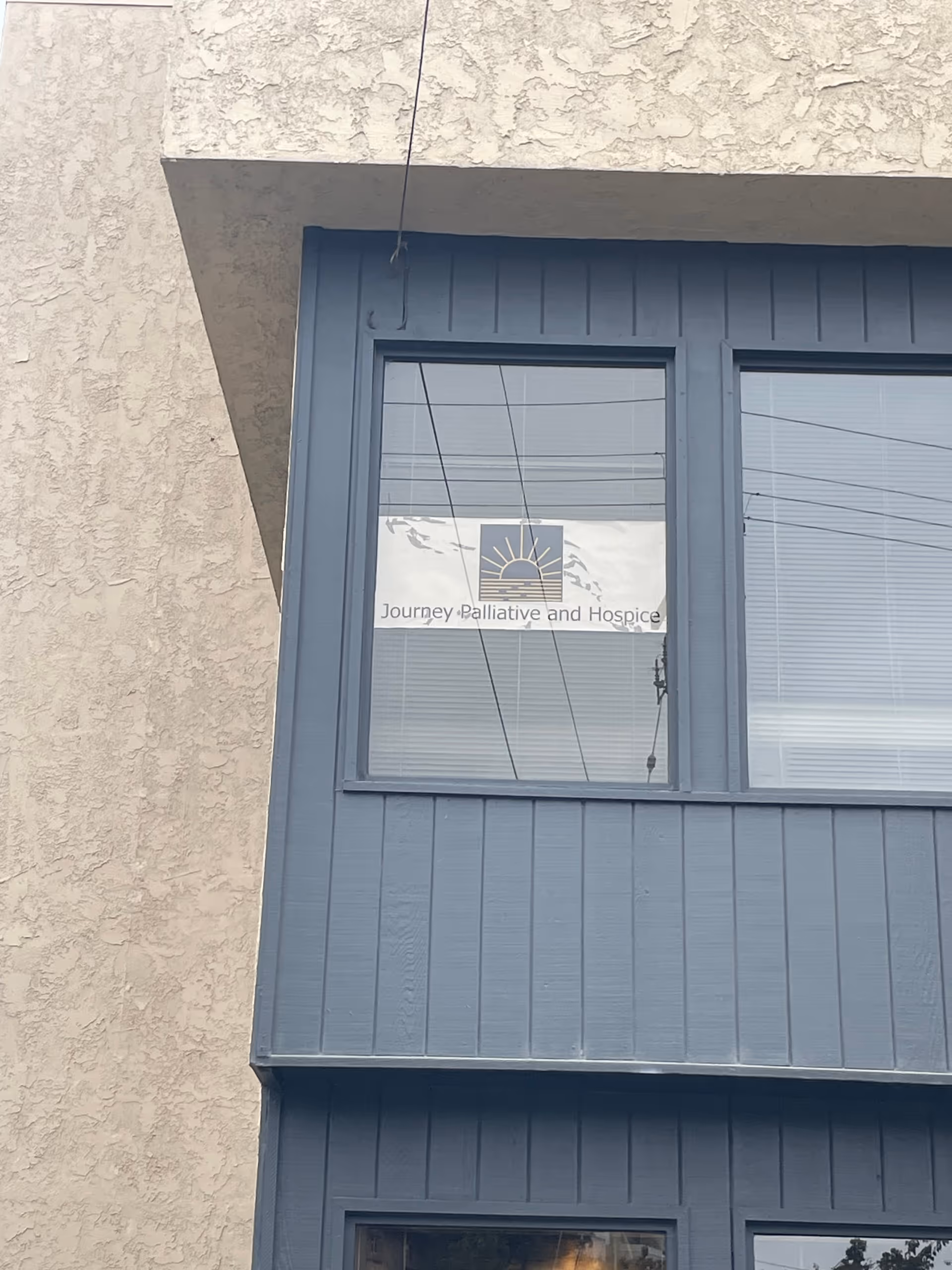 Blue-framed window on beige stucco wall displaying Journey Palliative and Hospice sign.