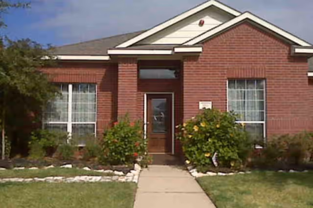 Single-story brick senior living facility exterior with front door and surrounding shrubs.