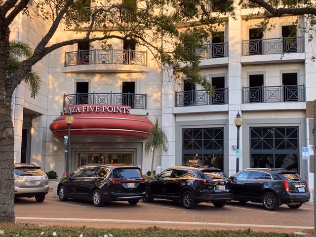 Exterior of a multi-story senior facility with a canopy entrance labeled Plaza Five Points and cars.