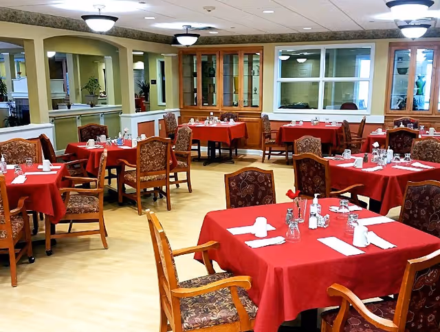 Dining room with multiple tables covered in red tablecloths, chairs, and place settings.
